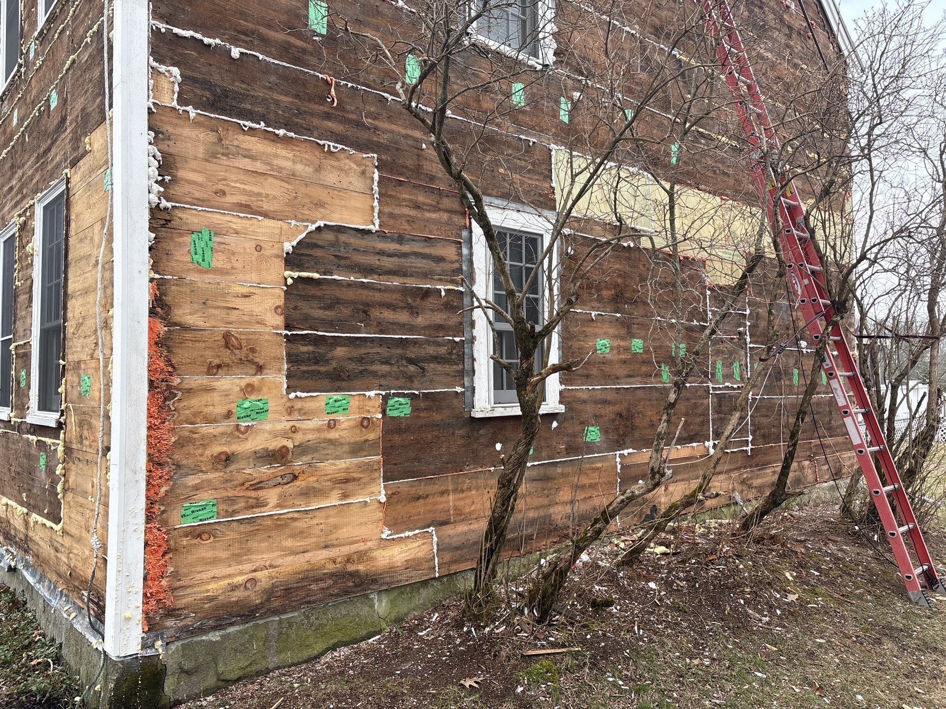 Weathered brick house with patched wood siding, white windows, and a red ladder leaning against the wall.