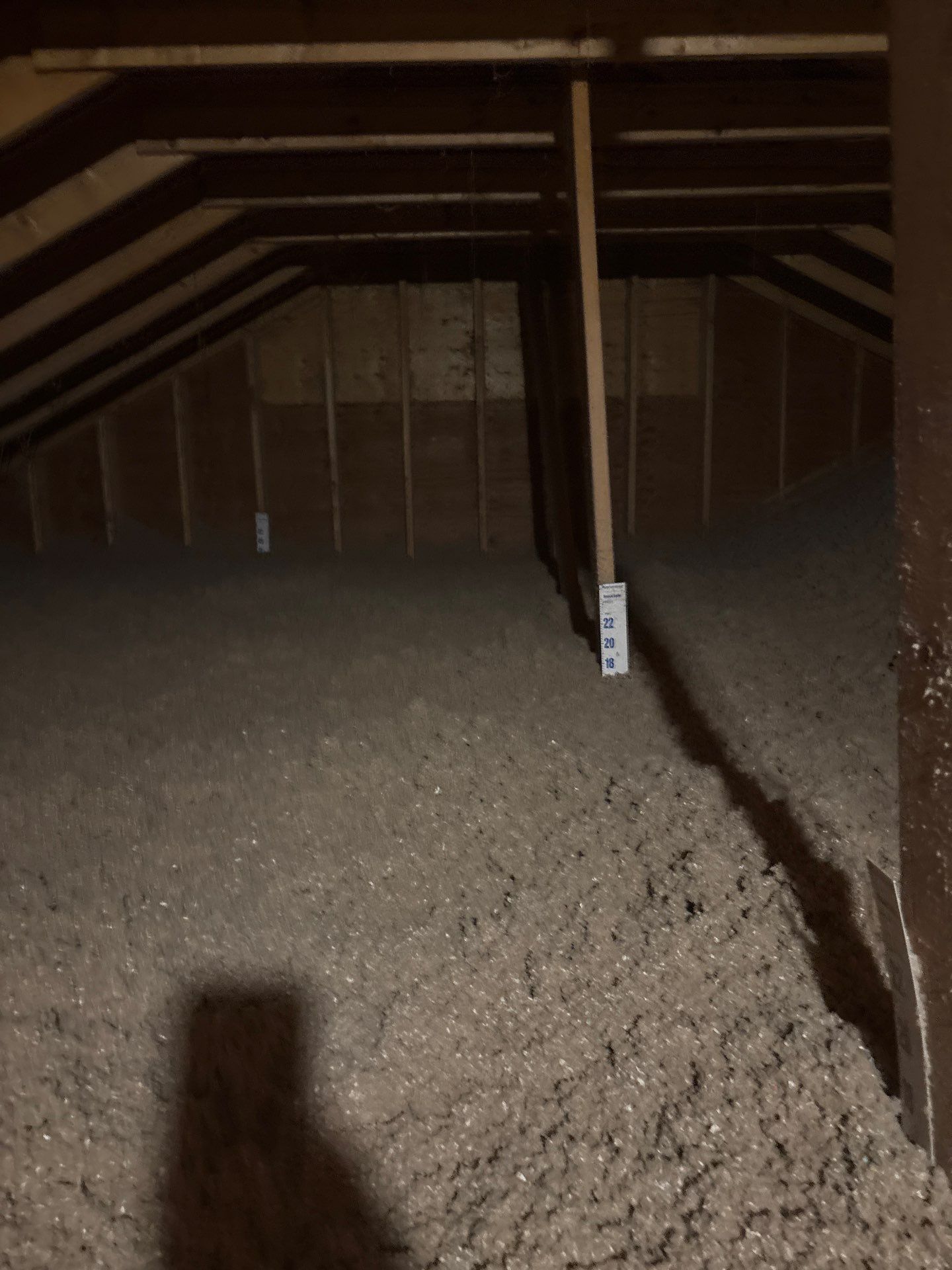 Dim attic with exposed rafters, insulation on the floor, and a central support post.