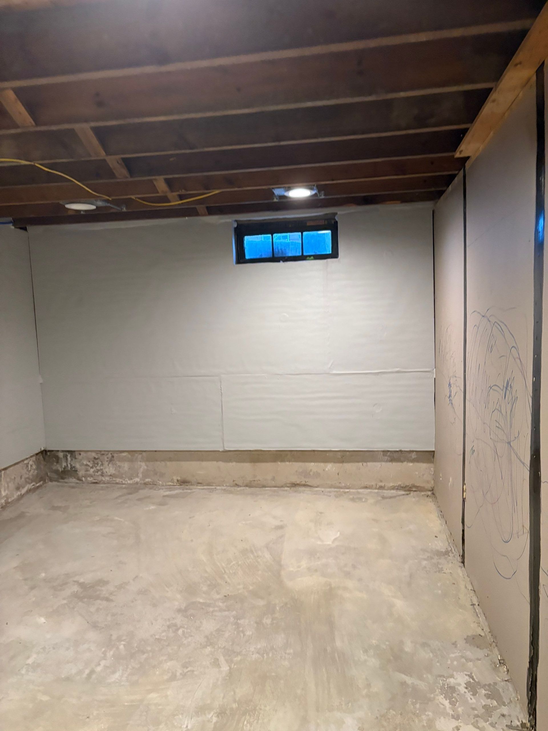 Empty unfinished basement with exposed ceiling joists, concrete floor, and small high window.