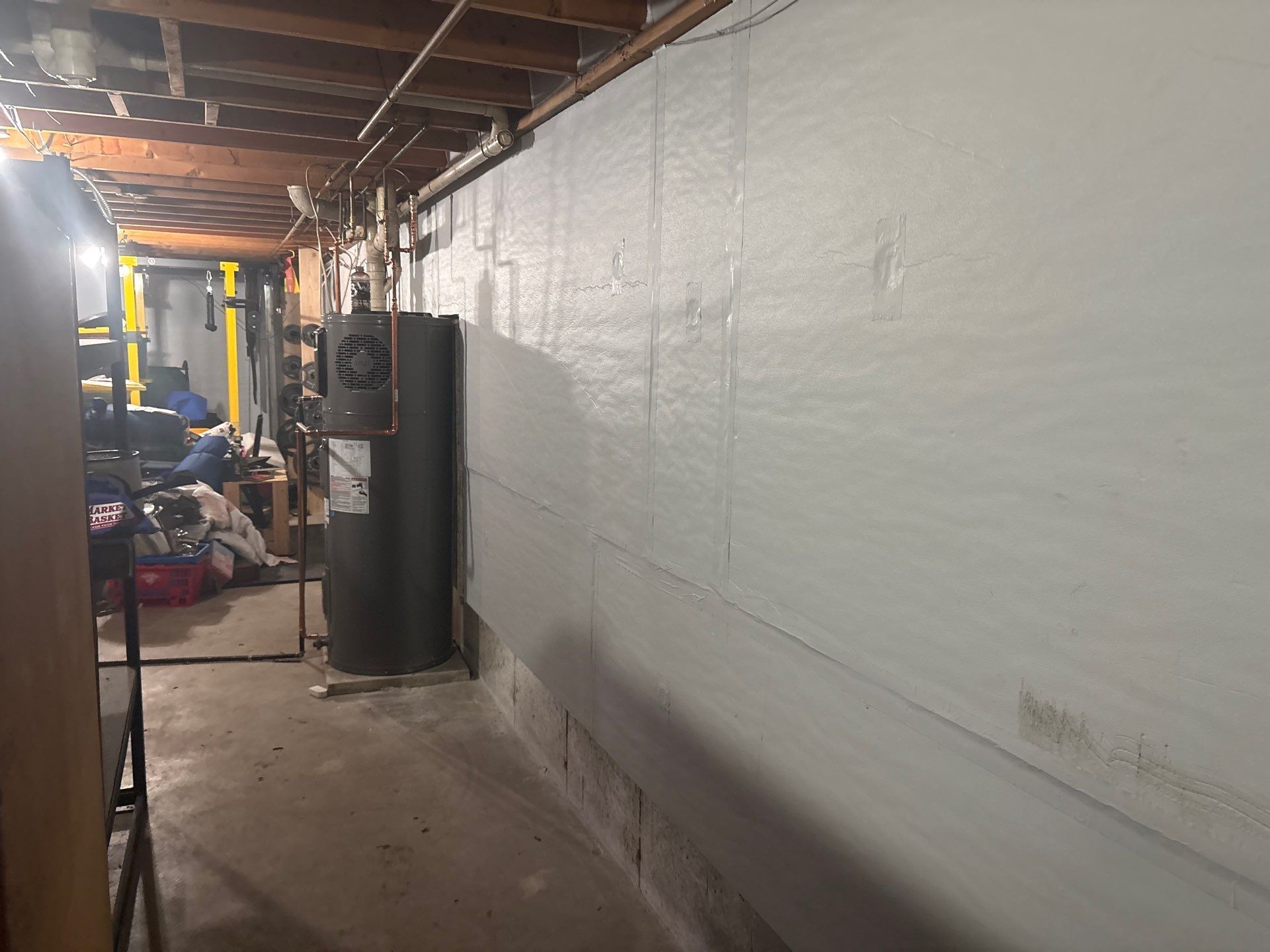 Narrow basement hallway with exposed beams, white painted wall, and a water heater at the end