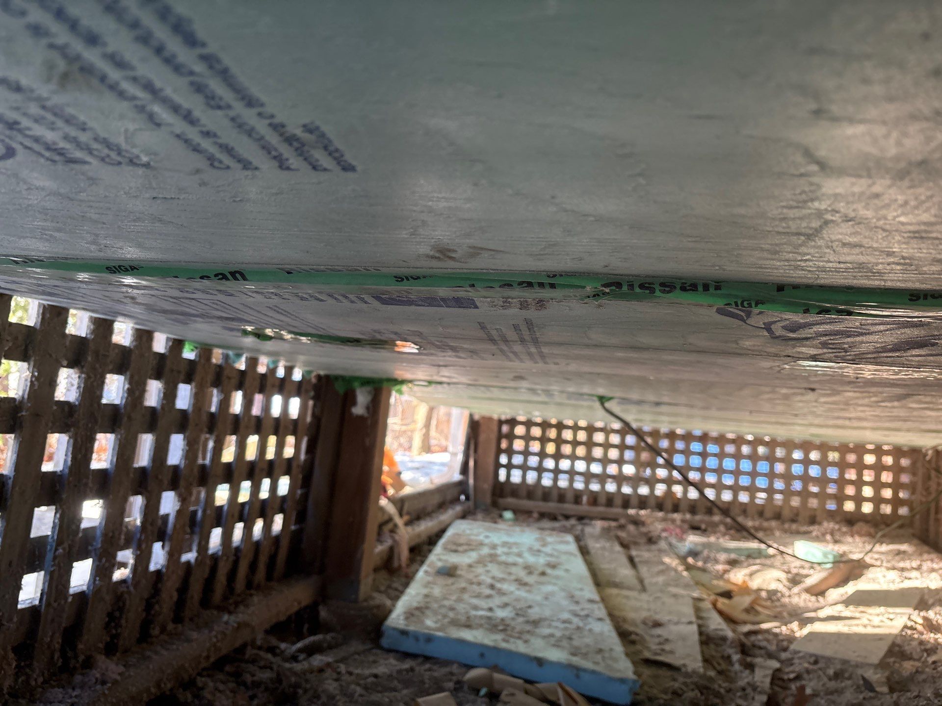 Under a raised structure with cinderblock vents, a mattress lies on a bare dirt floor.