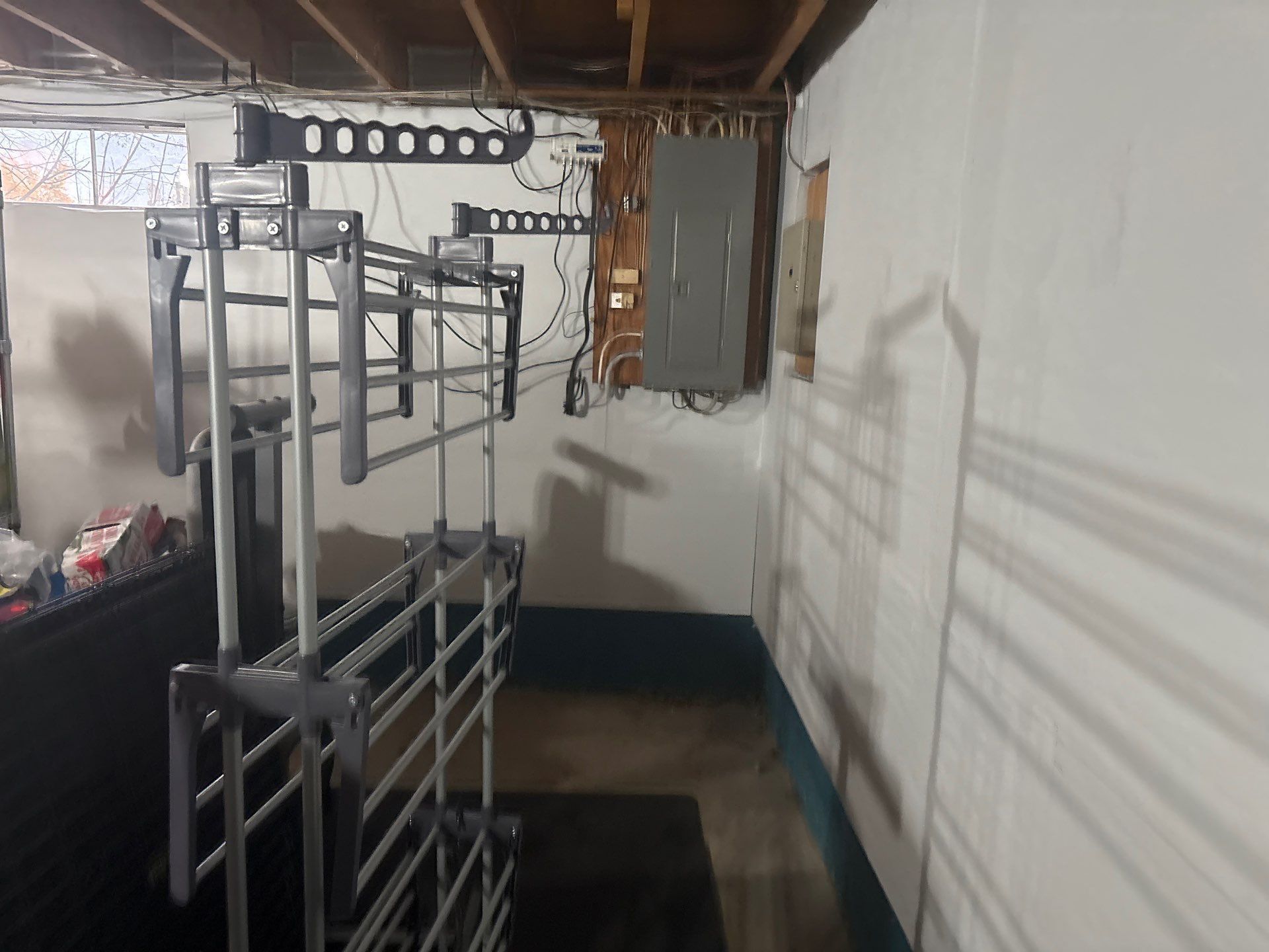 Narrow basement room with stacked metal bunk beds, white walls, and exposed wooden beams