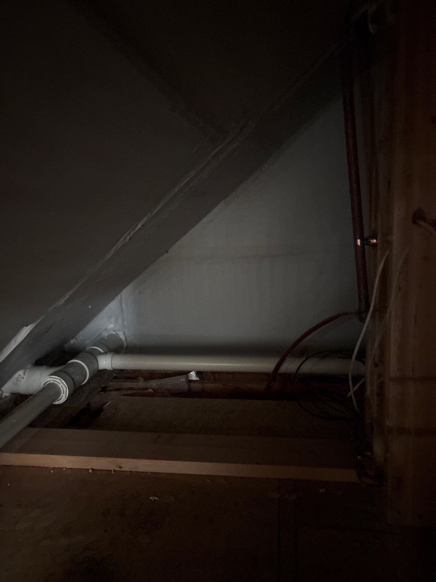 Dim attic crawlspace with exposed pipes, beams, and a slanted roof.