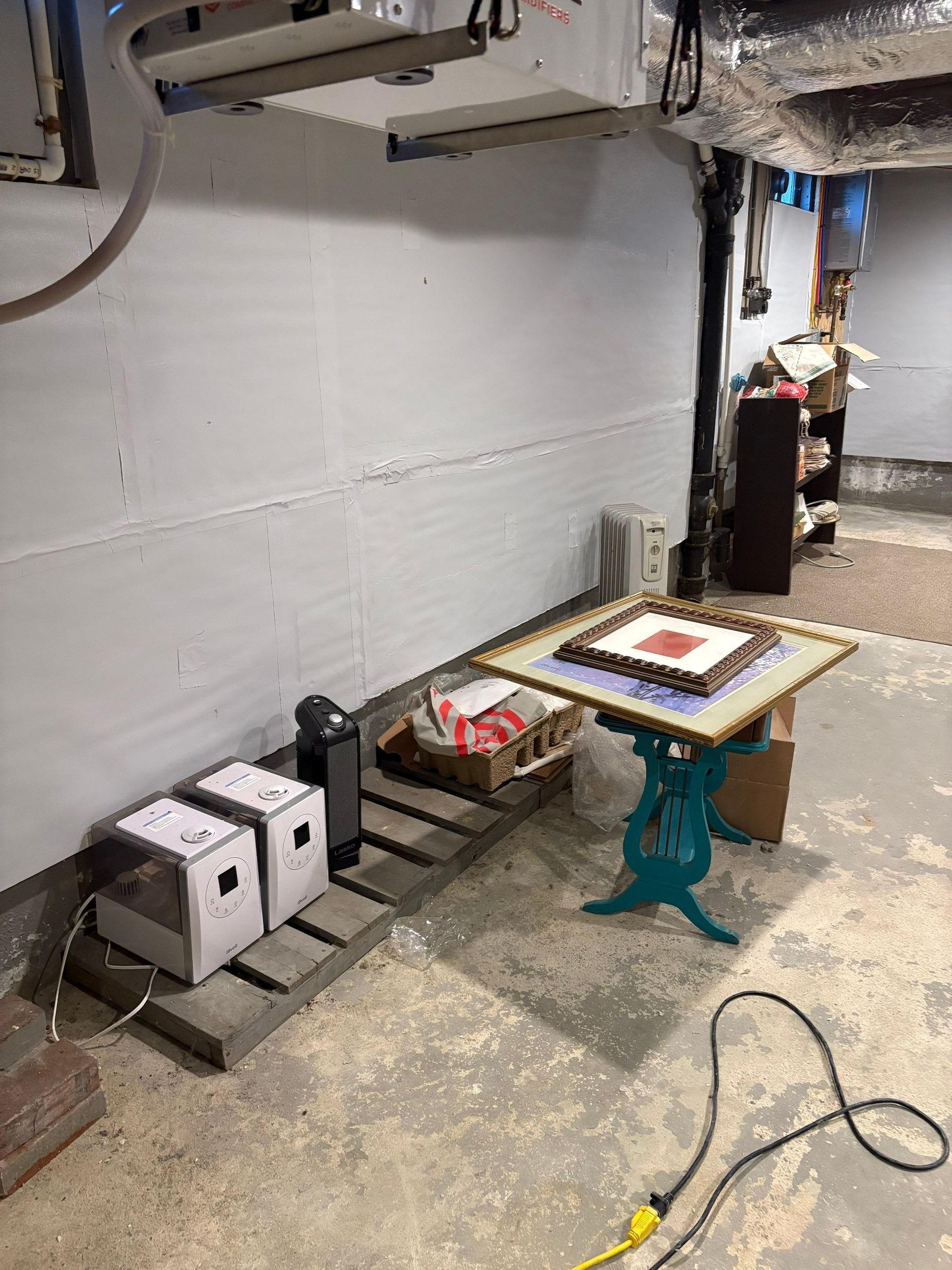 Garage workshop corner with black and white boxes, a small table, and a yellow cord on the floor.