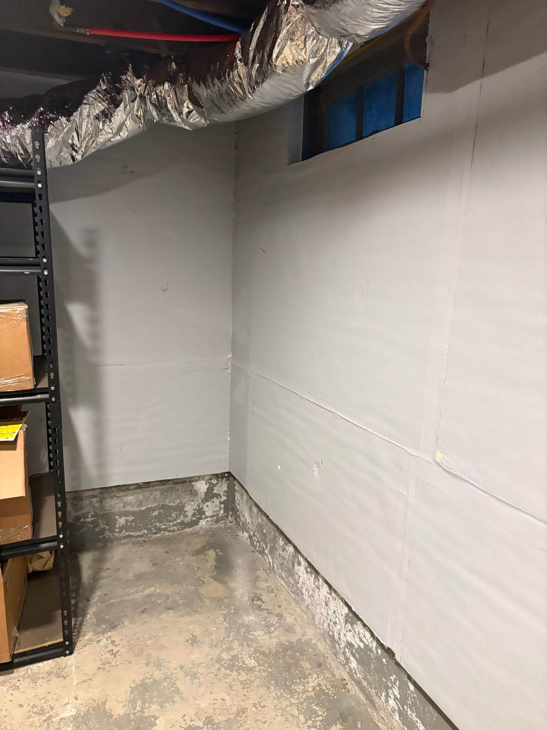 Small unfinished basement corner with white walls, exposed ductwork, and metal shelving on the left.