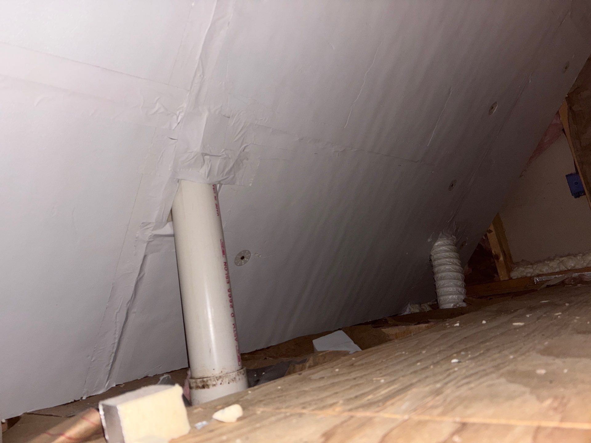 Attic interior with slanted white insulation, exposed pipes, and a wooden floorboard surface