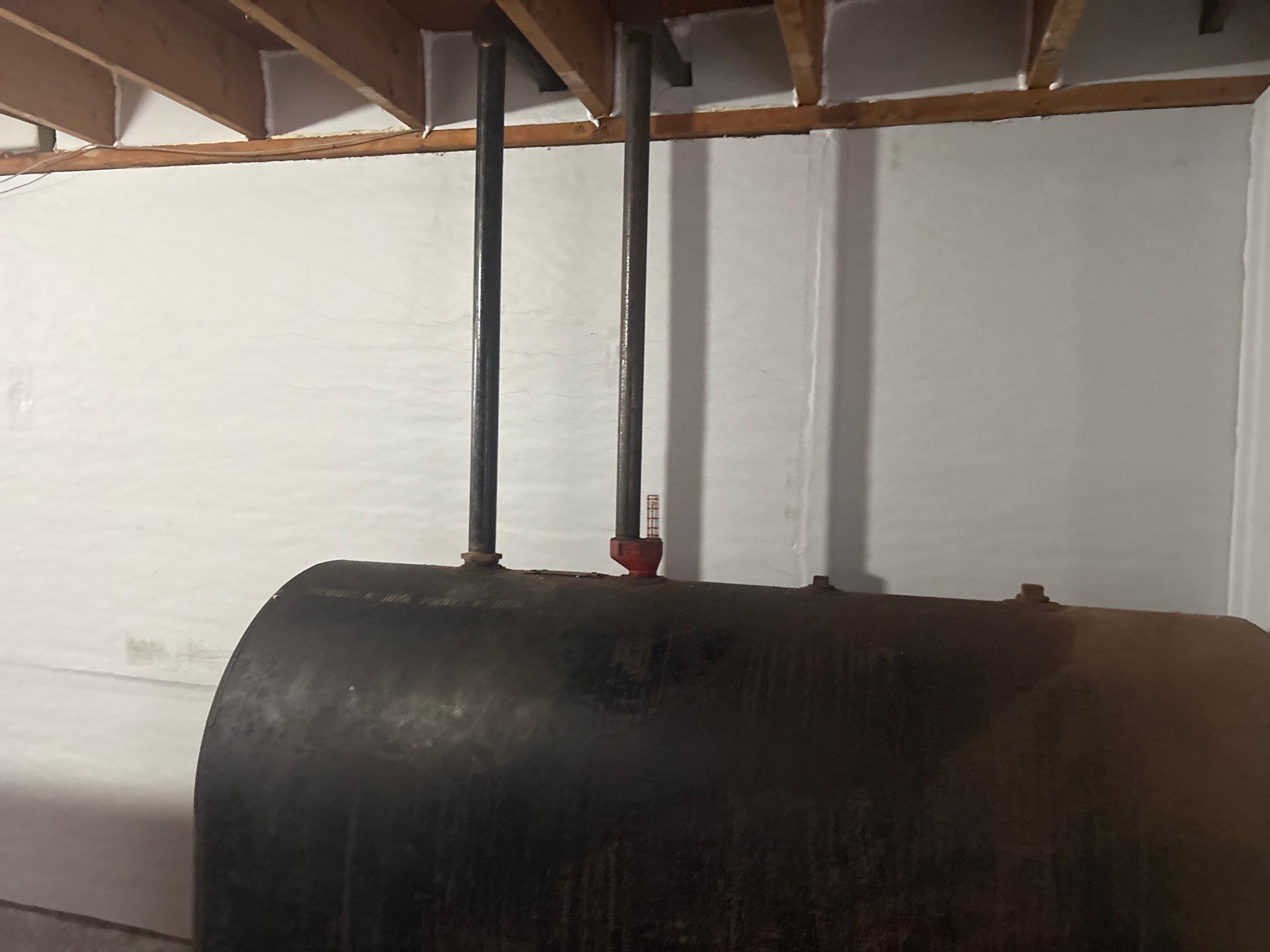 Black cylindrical tank with two pipes attached under a wooden ceiling indoors