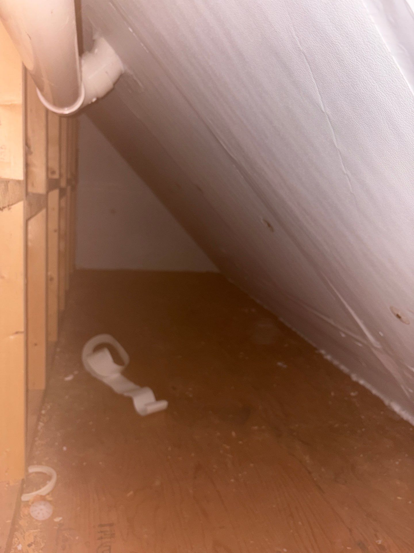 Cluttered attic corner with a slanted white wall, wooden floor, and a small white object on the floor
