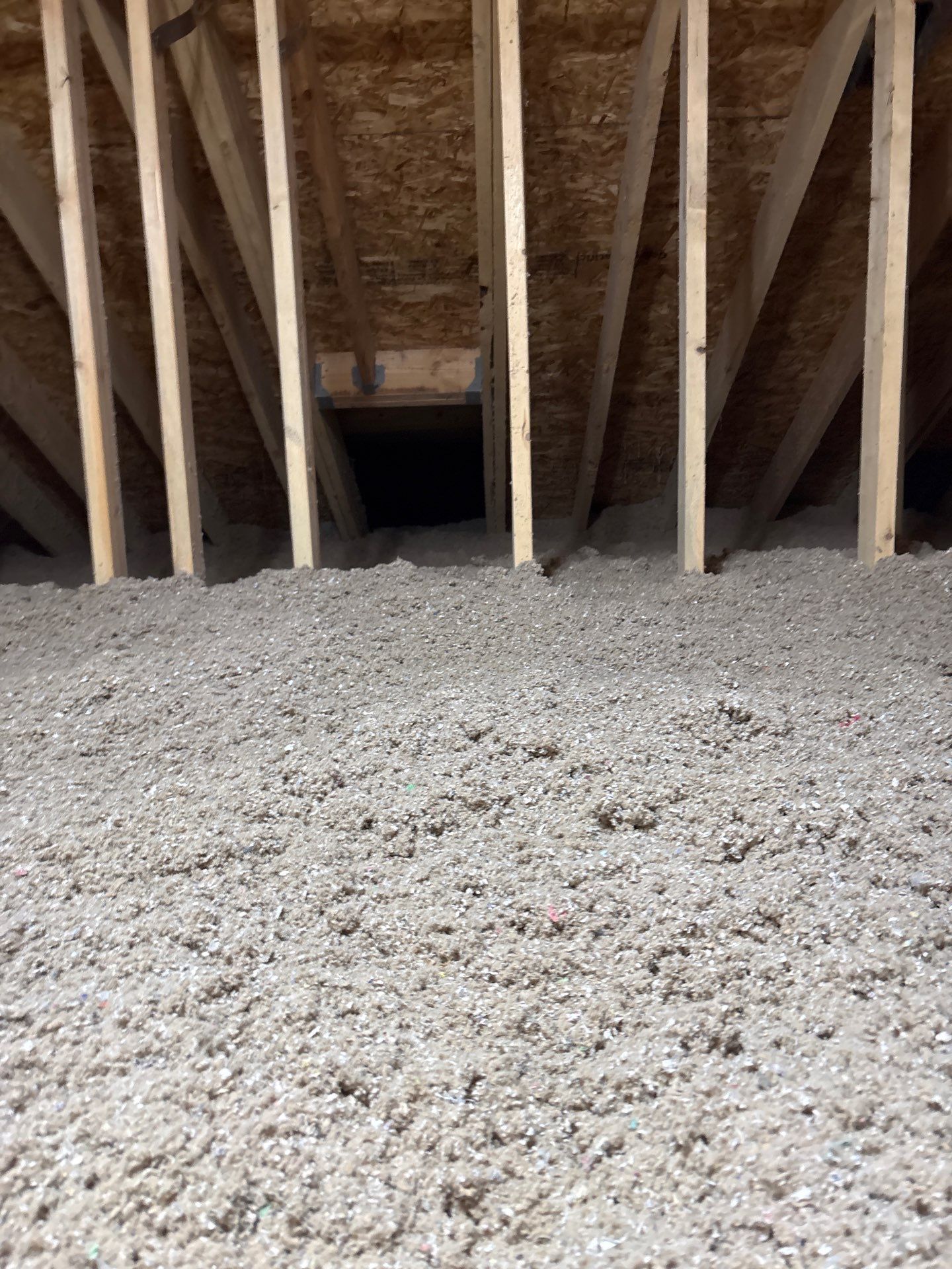 Exposed attic framing with sloped rafters and insulation over a gravel-covered floor, centered on a dark opening