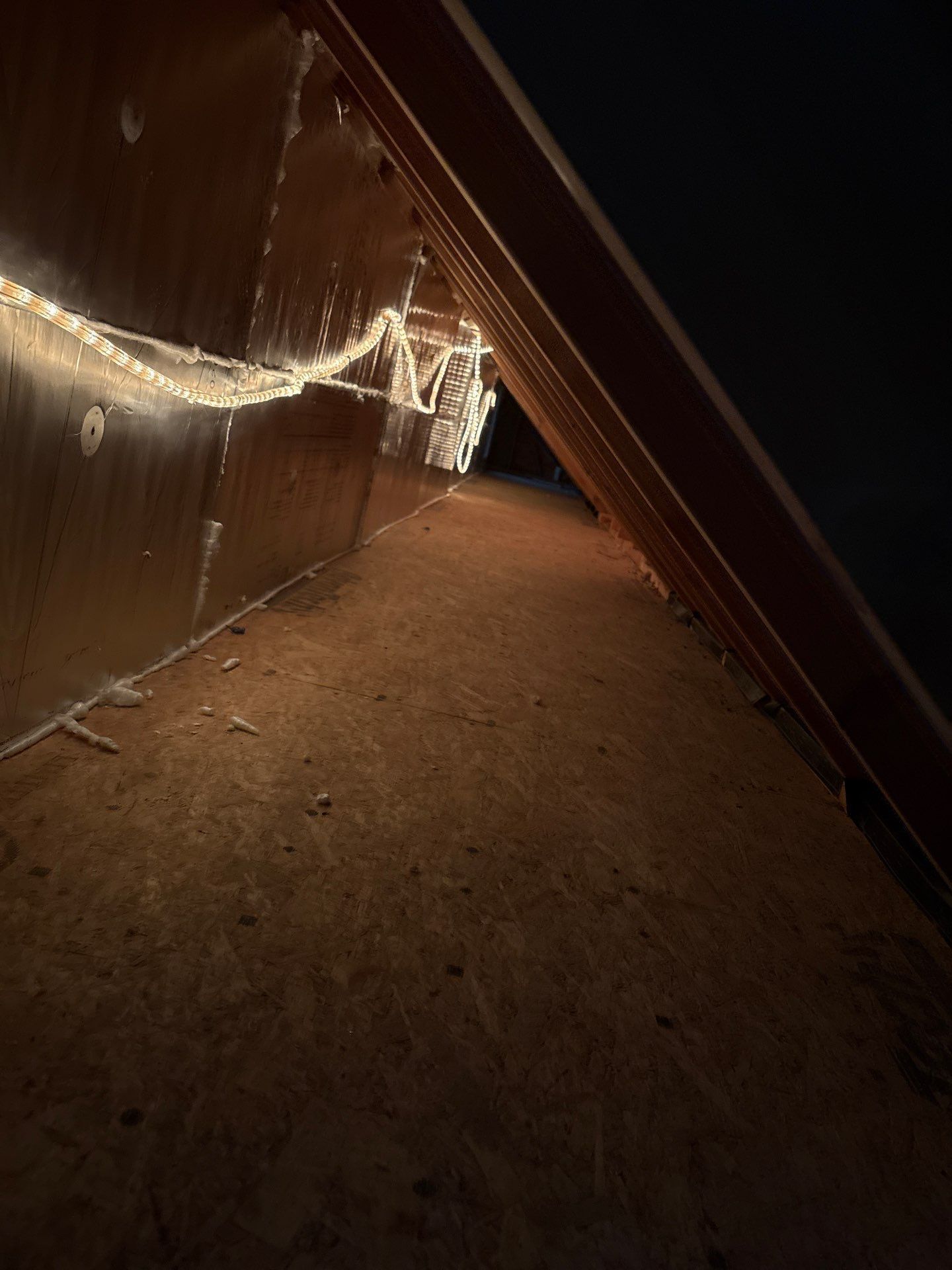 Night view of a steep dirt slope beside a corrugated metal wall with string lights.