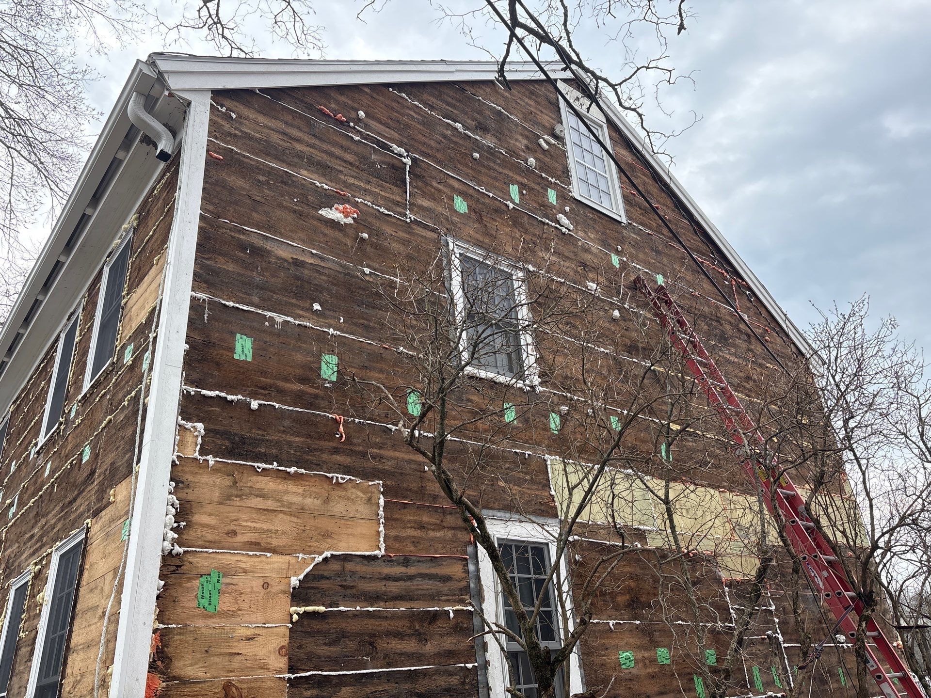 Weathered brick house with peeling paint and cracked facade, seen from below against a cloudy sky