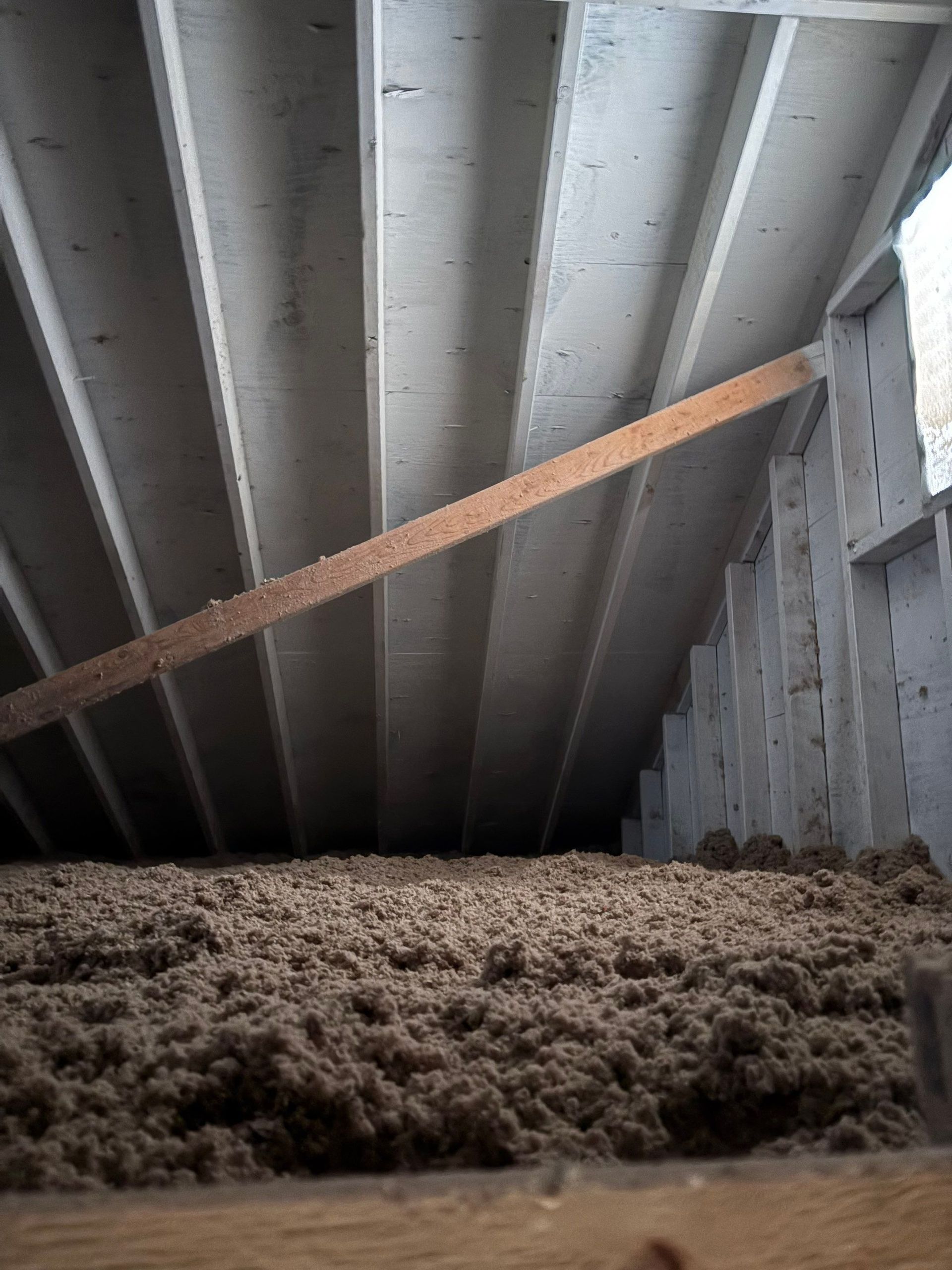 Low-angle view of attic insulation beneath gray roof beams with a diagonal wooden brace
