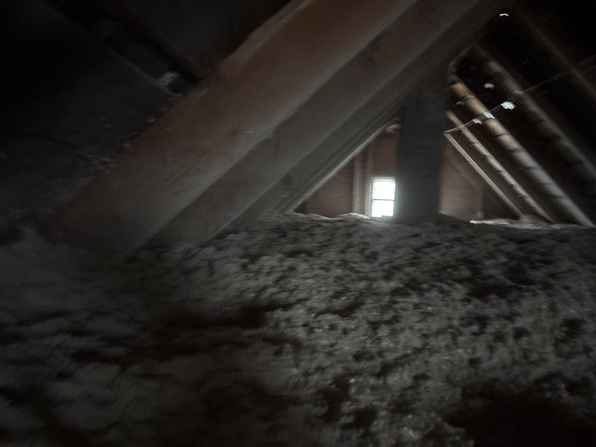 Dim attic interior with wooden rafters and a large pile of insulation or debris on the floor.