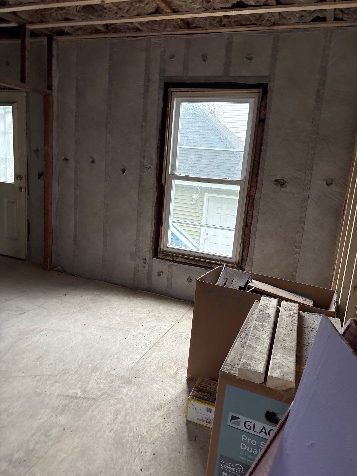 Unfinished room with exposed insulation, a window, and cardboard boxes on the floor.