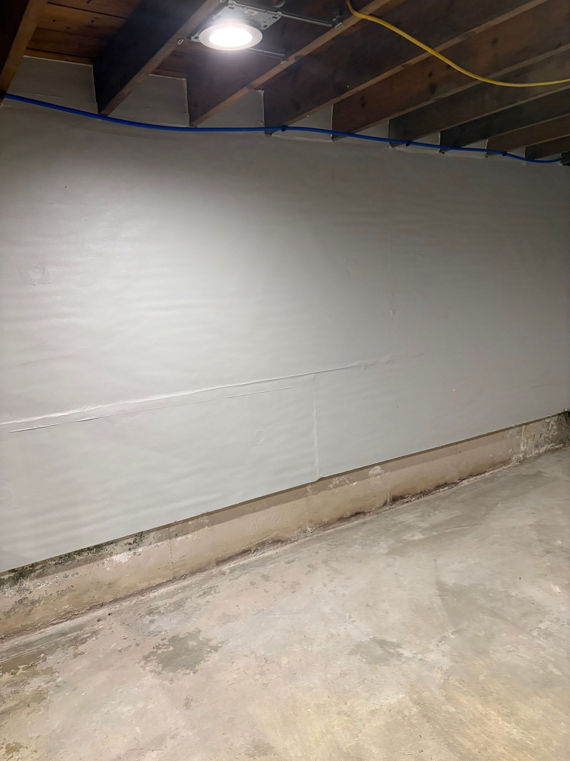 Dim unfinished basement wall with exposed ceiling and concrete floor, lit by a single overhead light
