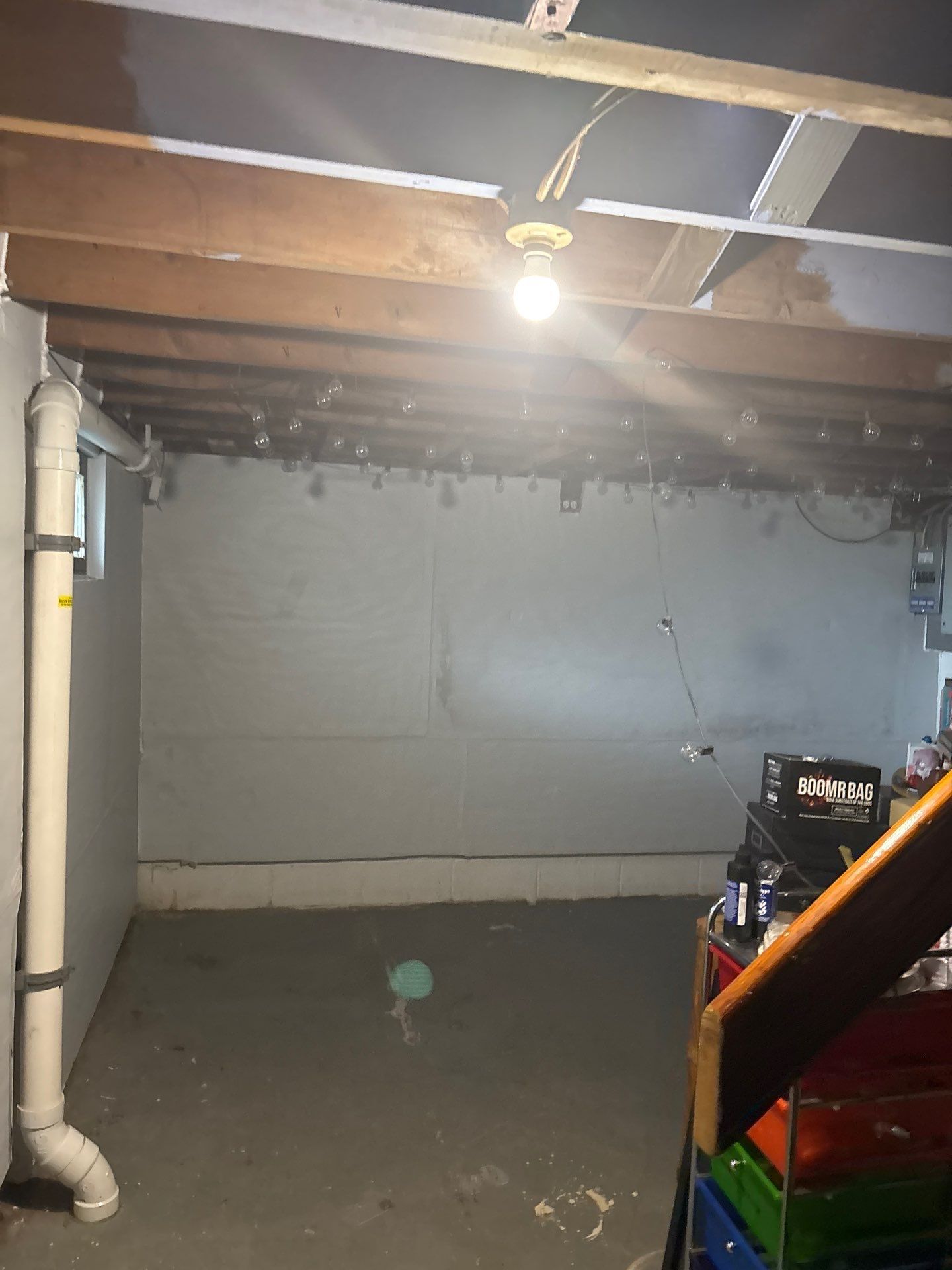 Dim unfinished basement with exposed ceiling beams, concrete floor, and a lit bare bulb.