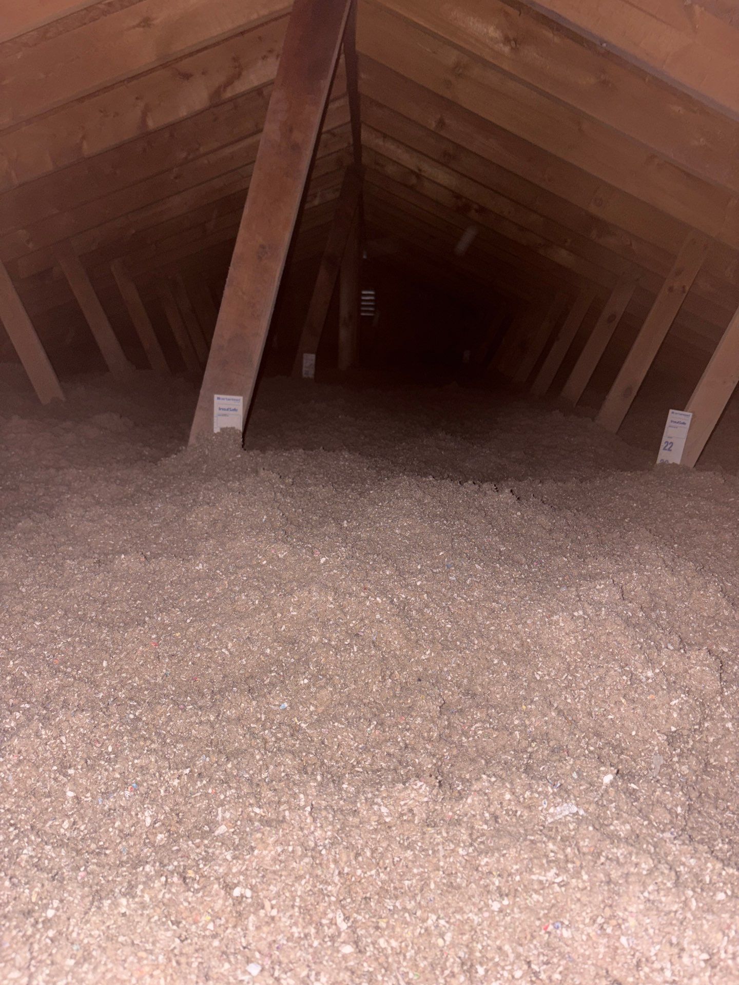 Empty attic with exposed wooden beams and a floor covered in insulation.