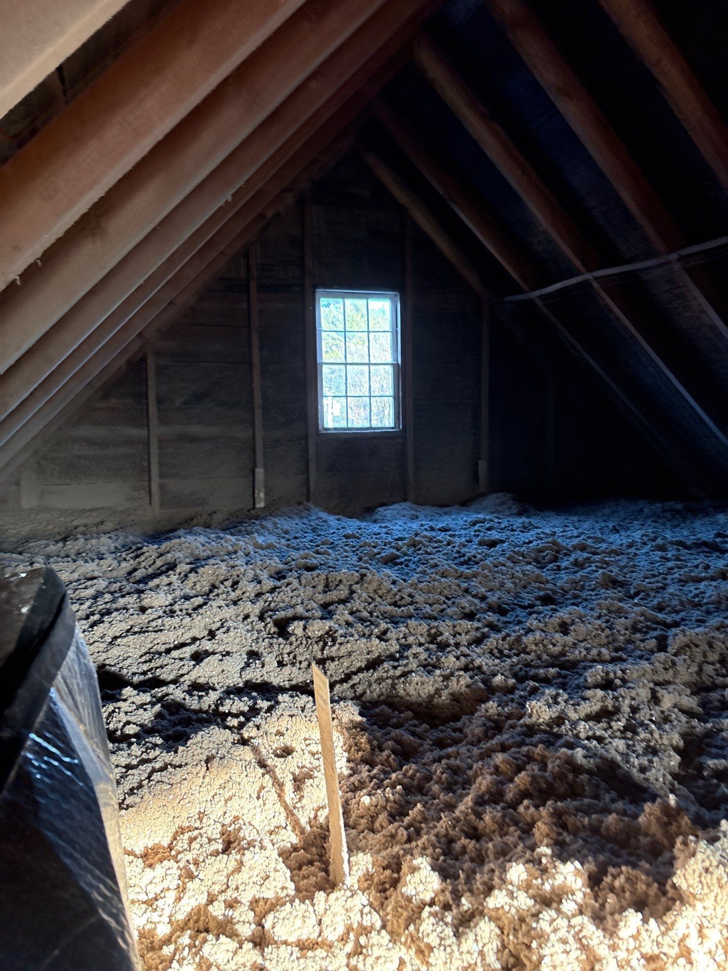 Attic with exposed rafters, insulation on the floor, and a small window at the far end