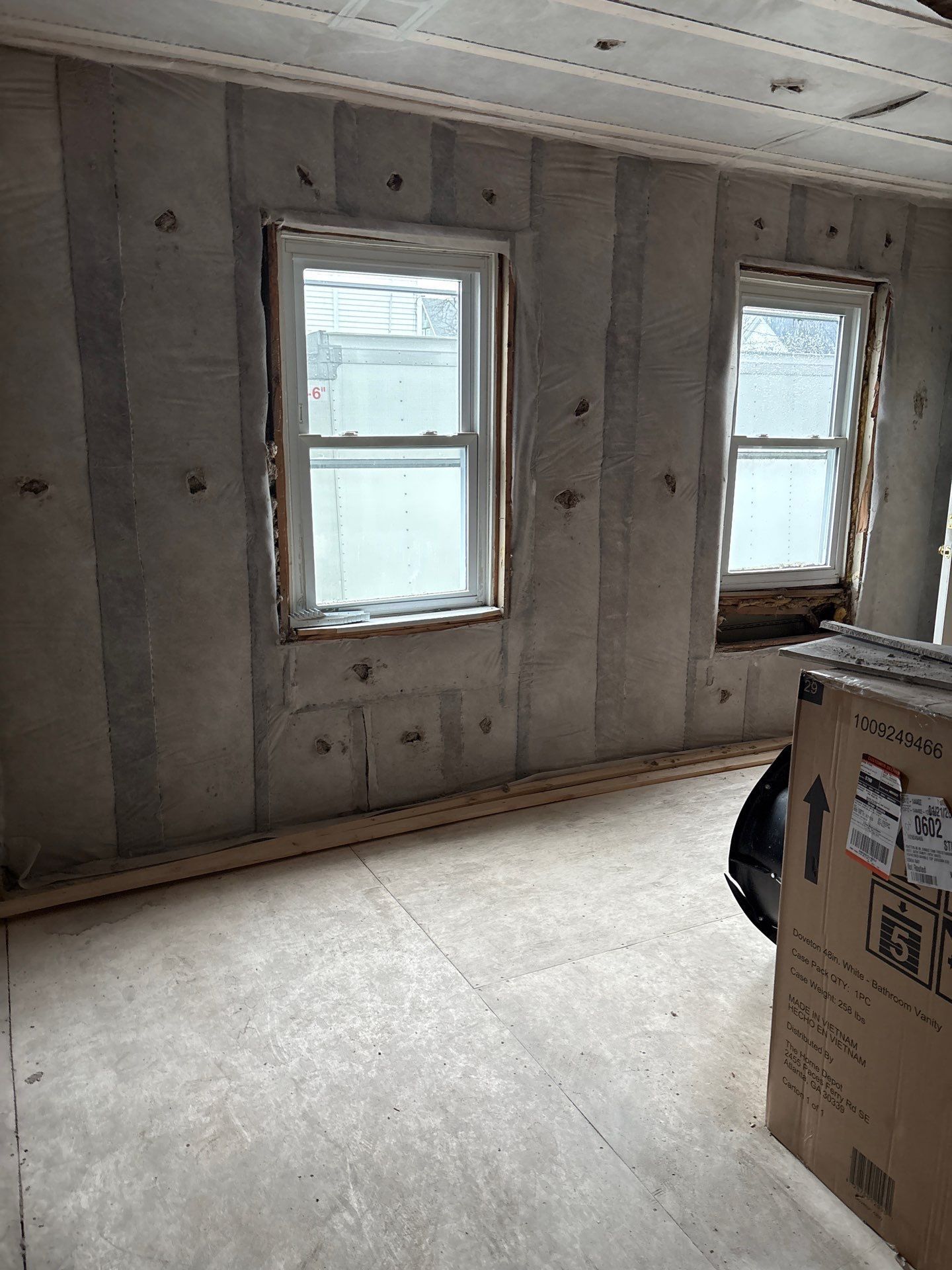 Unfinished room with exposed concrete walls, two windows, and a cardboard box on the floor.