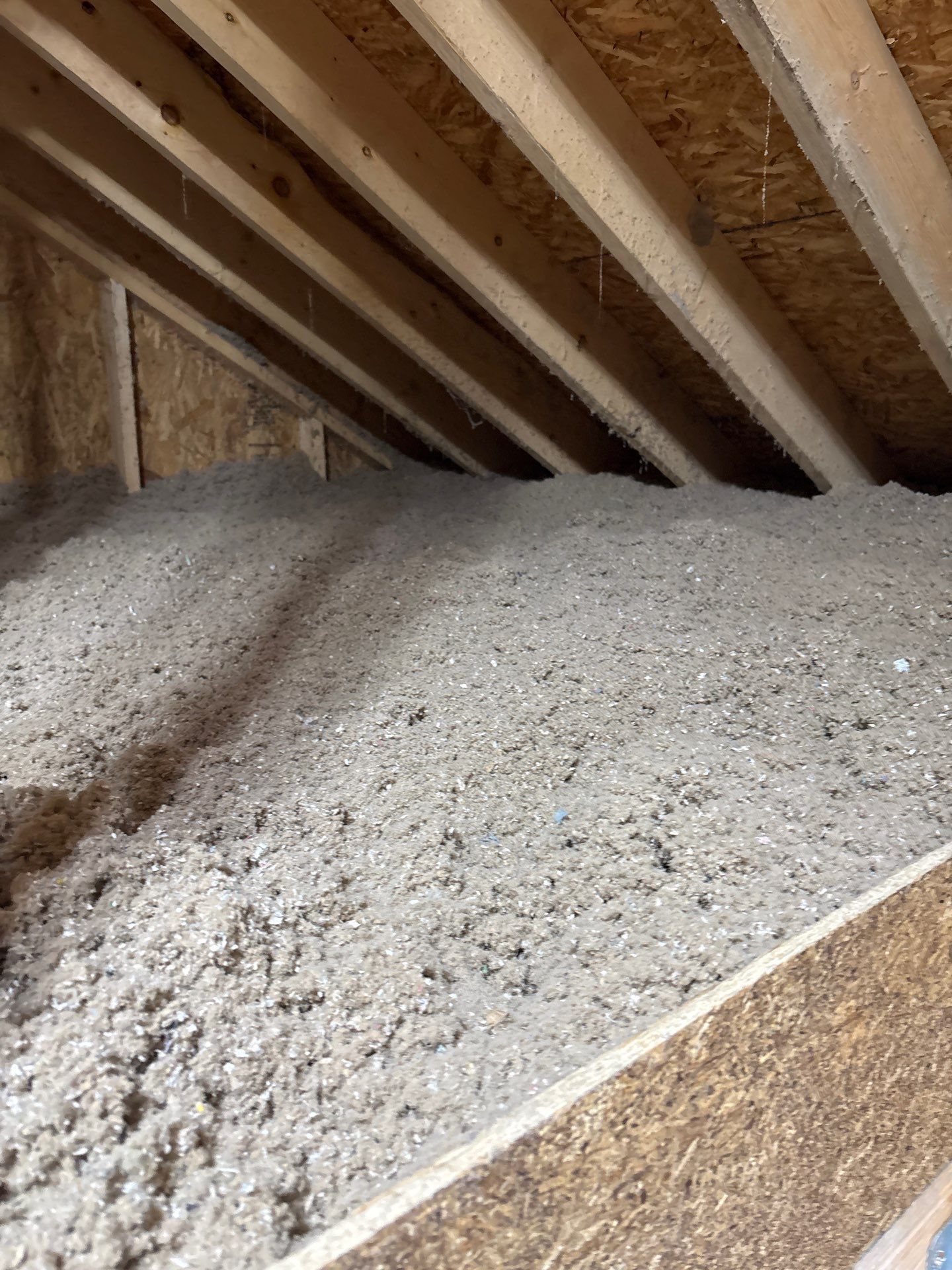 Attic insulation piled beneath exposed wooden rafters and roof decking