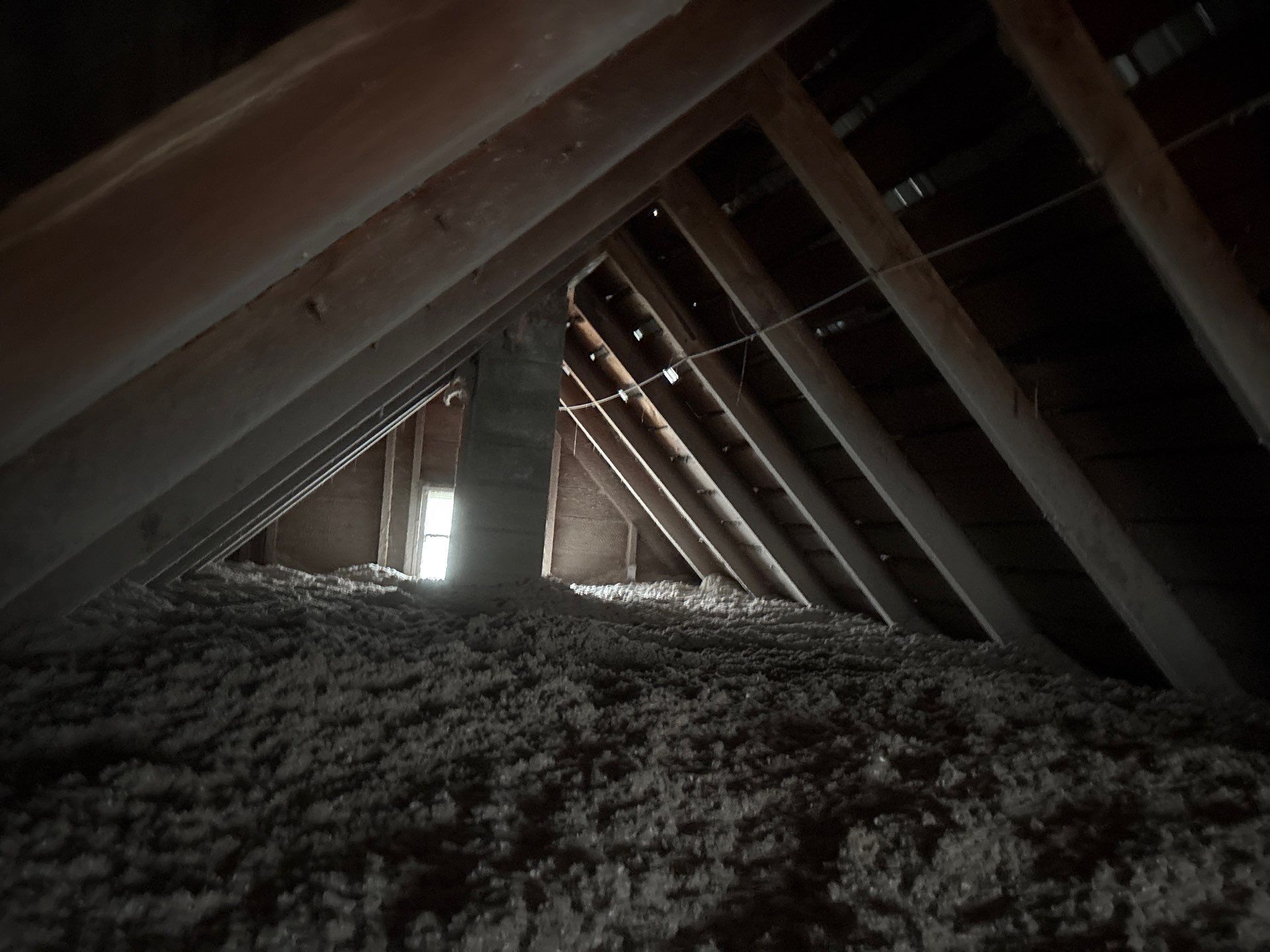 Interior of an attic with exposed wooden rafters and a narrow opening of daylight at the far end