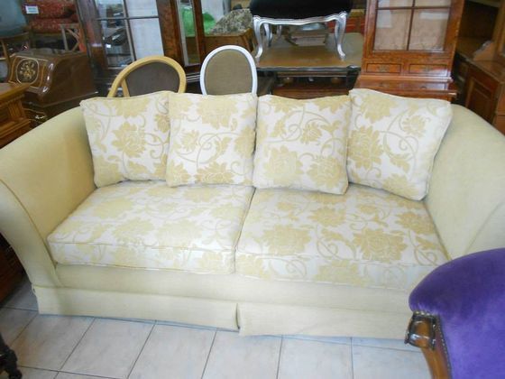 Sofá color crema con estampado floral y cojines a juego en una sala de estar, con una silla morada en el extremo.