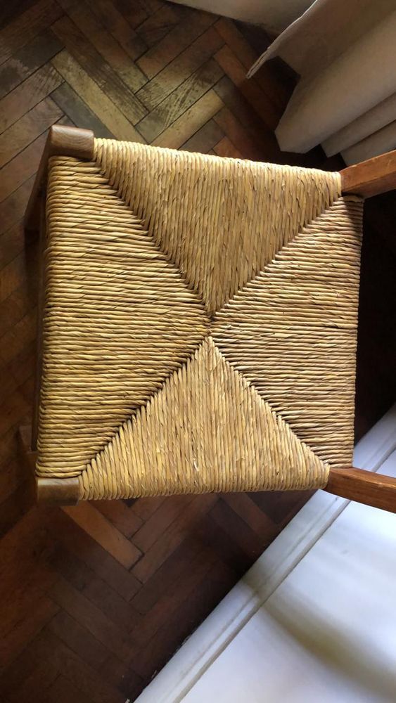 Vista superior de un taburete cuadrado de paja tejida con un estampado geométrico sobre un suelo de madera.