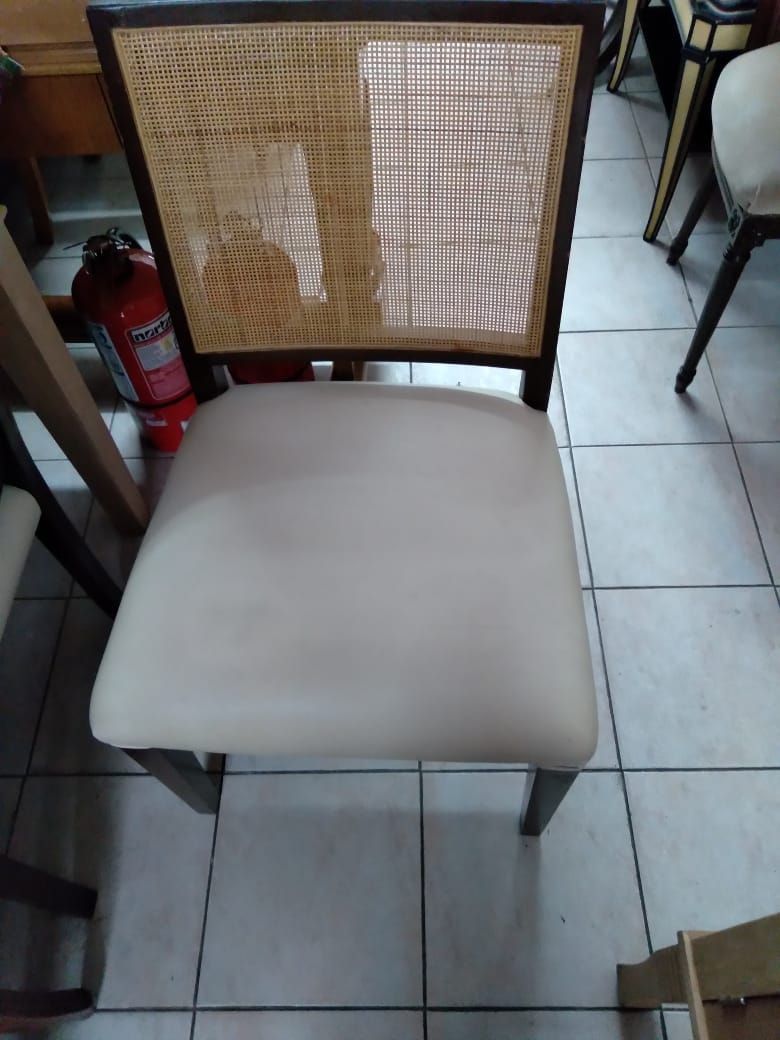 Silla beige acolchada con respaldo de madera tejida sobre un suelo de baldosas en el interior.