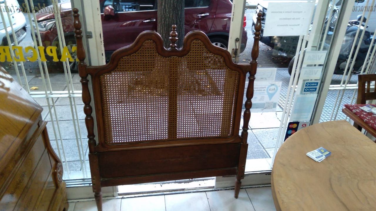 Banco de mimbre con respaldo de madera tallada en el escaparate de una tienda de muebles, con mesas y armarios cerca.