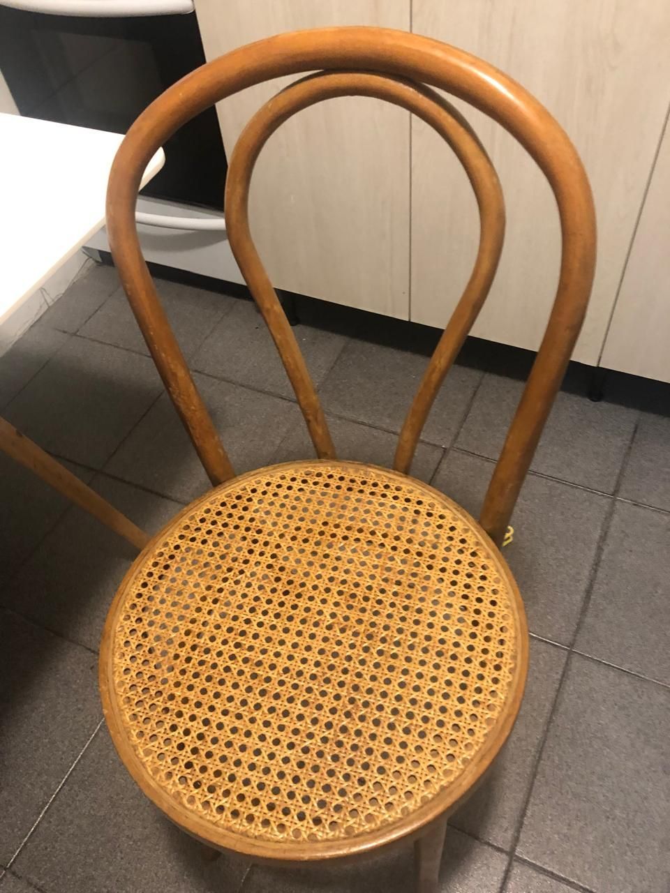 Silla de madera curvada con asiento tejido en un rincón de la cocina sobre un suelo de baldosas.