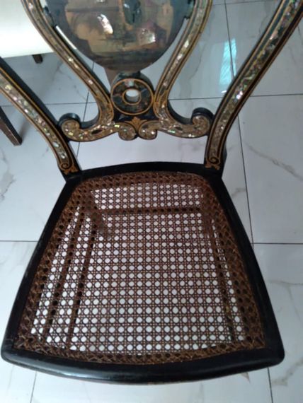Silla con asiento de caña tejida, estructura de madera oscura y respaldo curvo en una habitación alicatada.