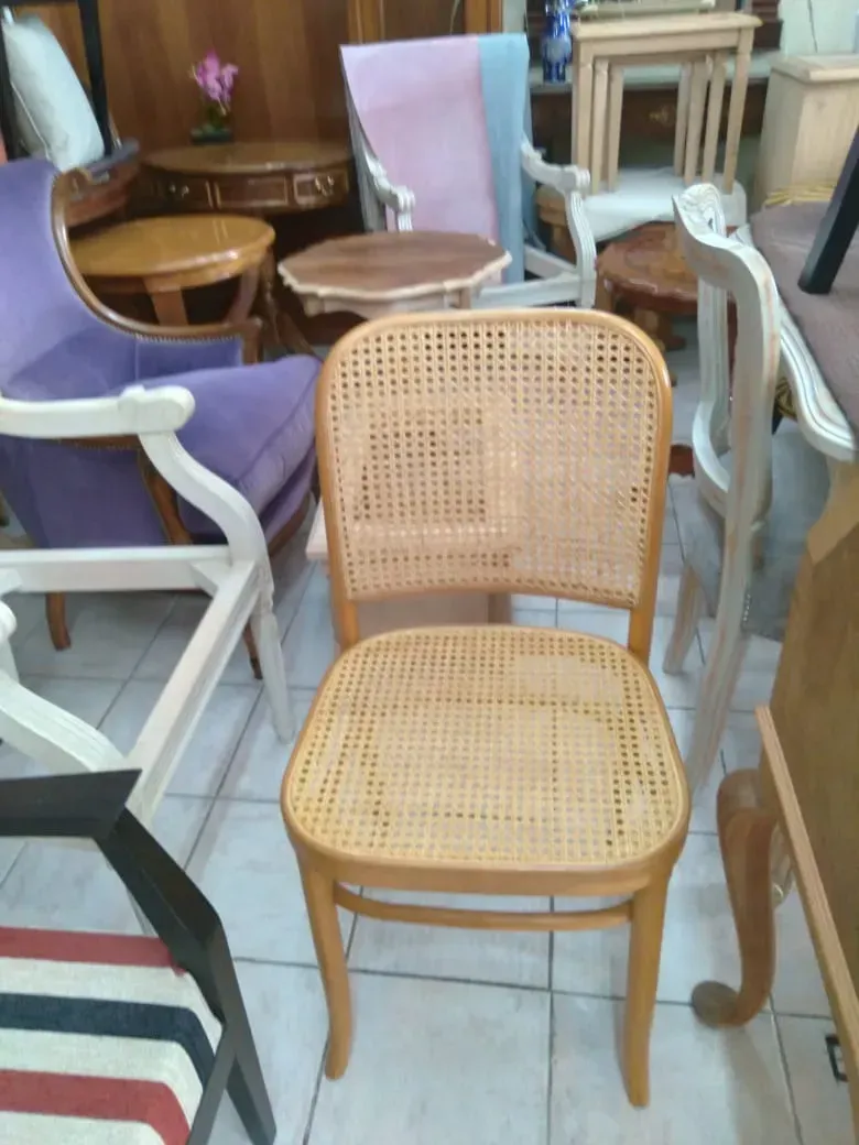 Silla de caña tejida en el centro, entre sillas variadas, en una abarrotada sala de exposición de muebles.