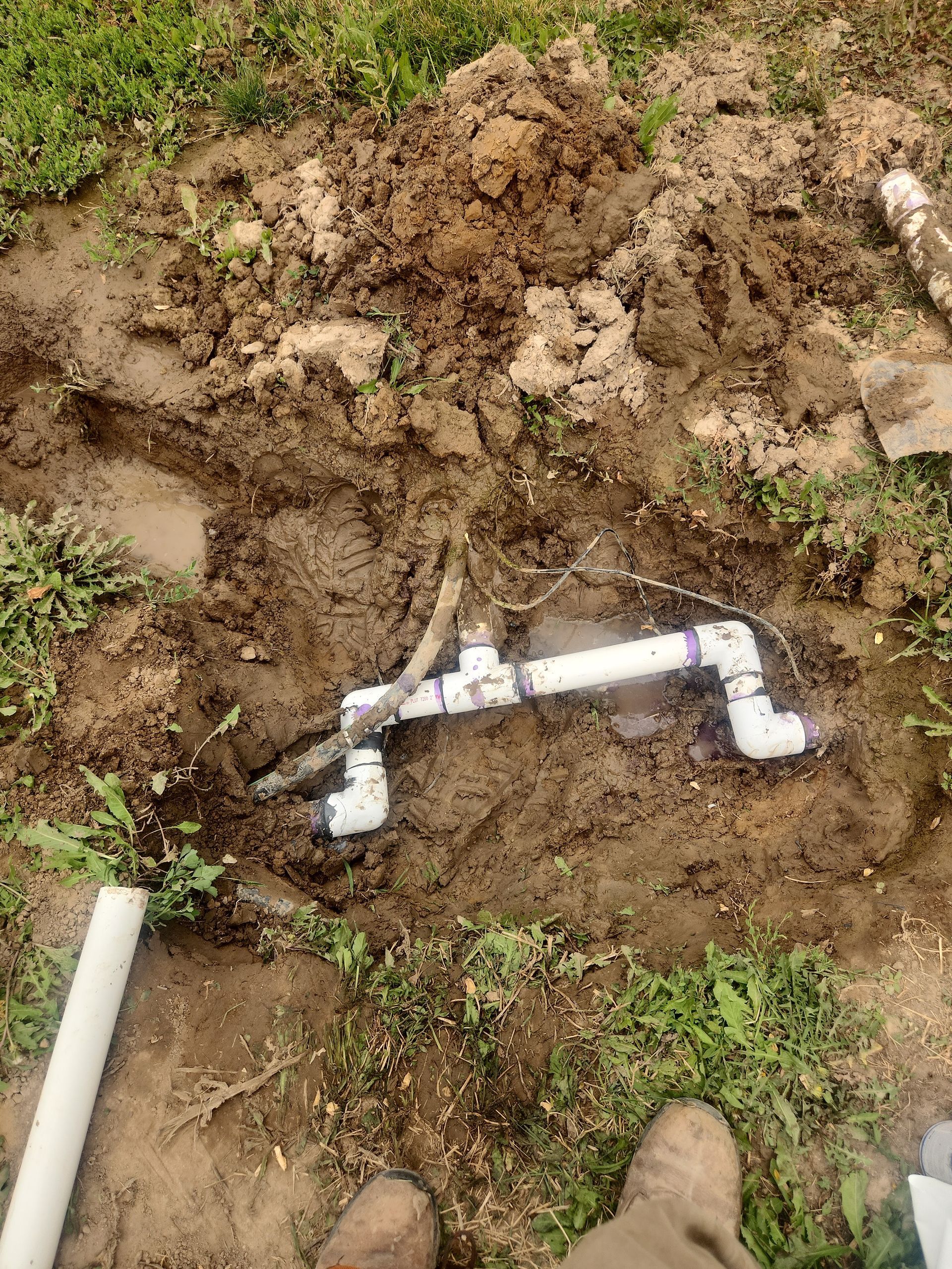 PVC pipe irrigation system partially buried in muddy ground.