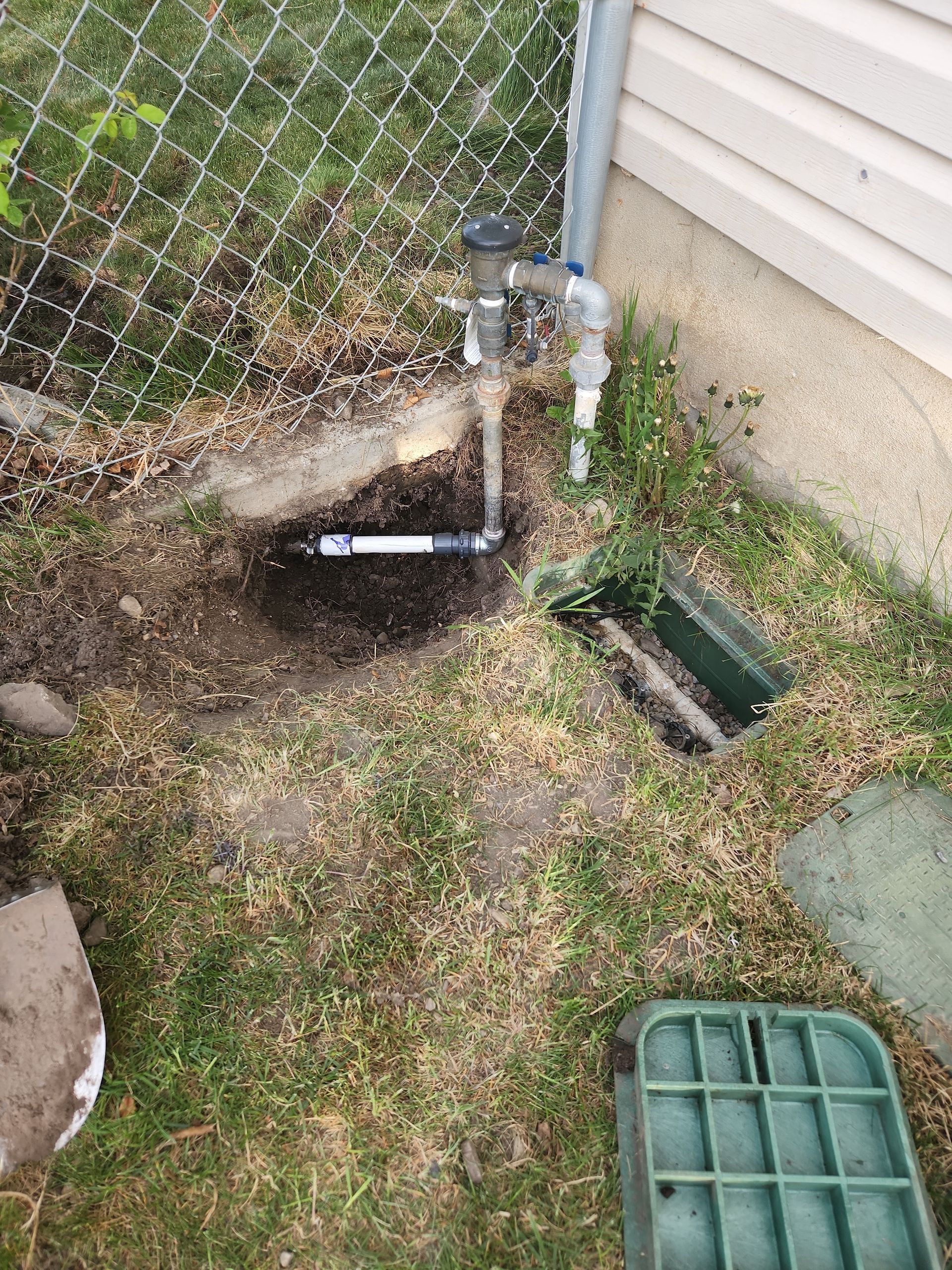 Irrigation system components: valves, pipes, and control box in a yard with sparse grass.