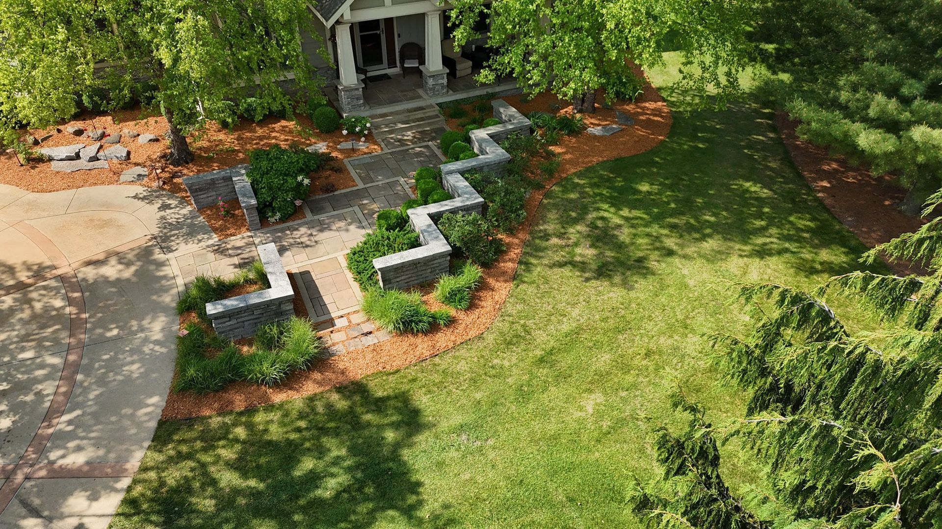 Aerial view of a home with a zig-zag stone retaining wall bordering a walkway and landscaped beds