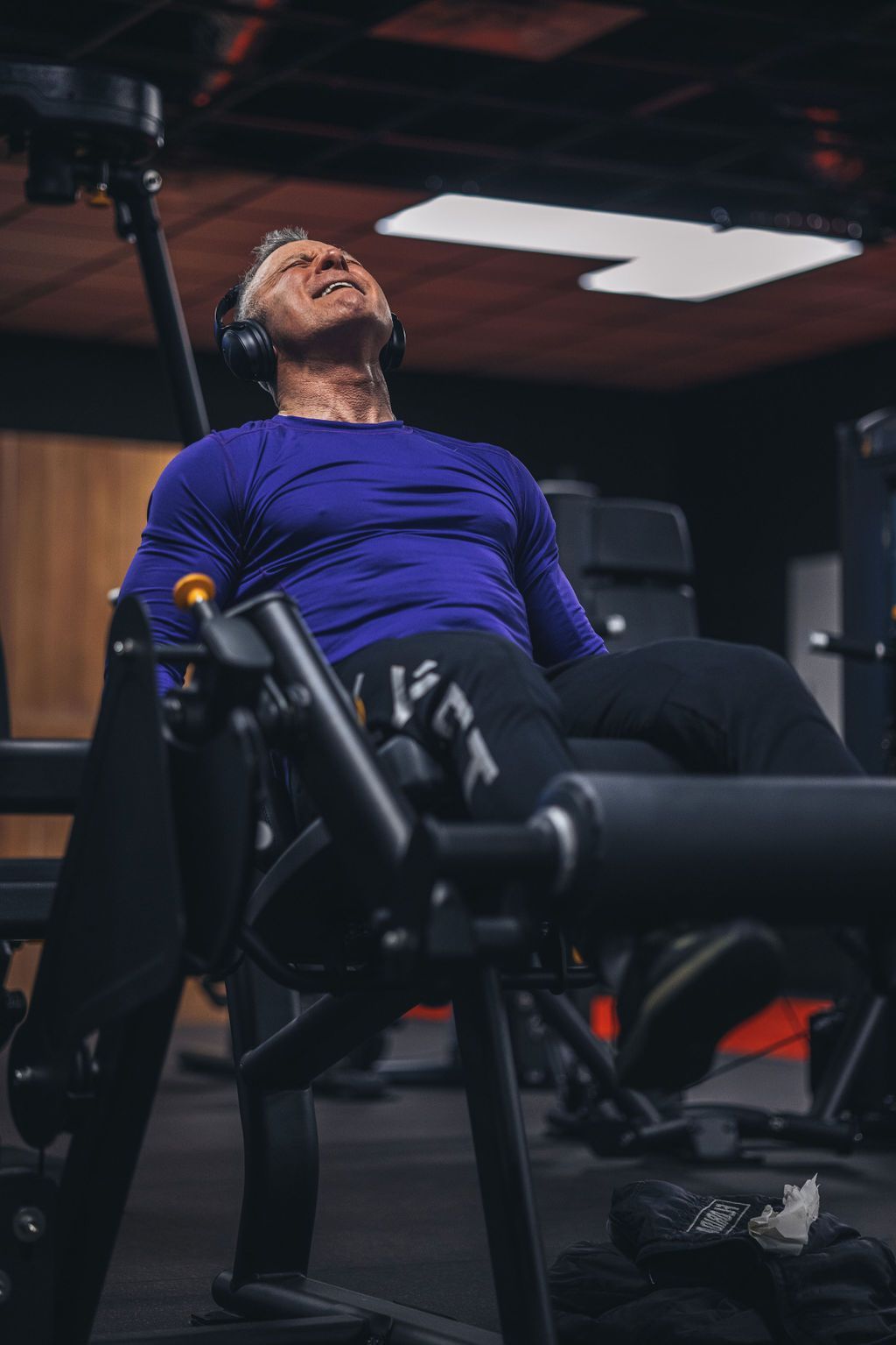 A man is laying on a leg extension machine in a gym.
