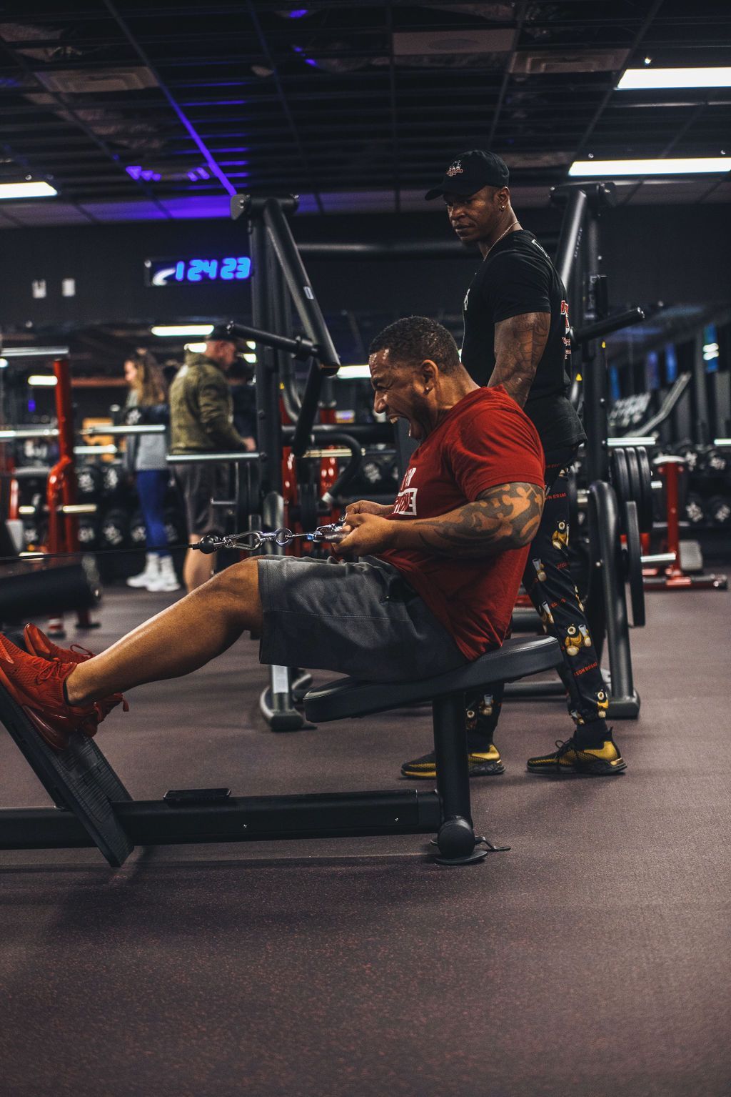 A man is sitting on a bench in a gym looking at his phone.