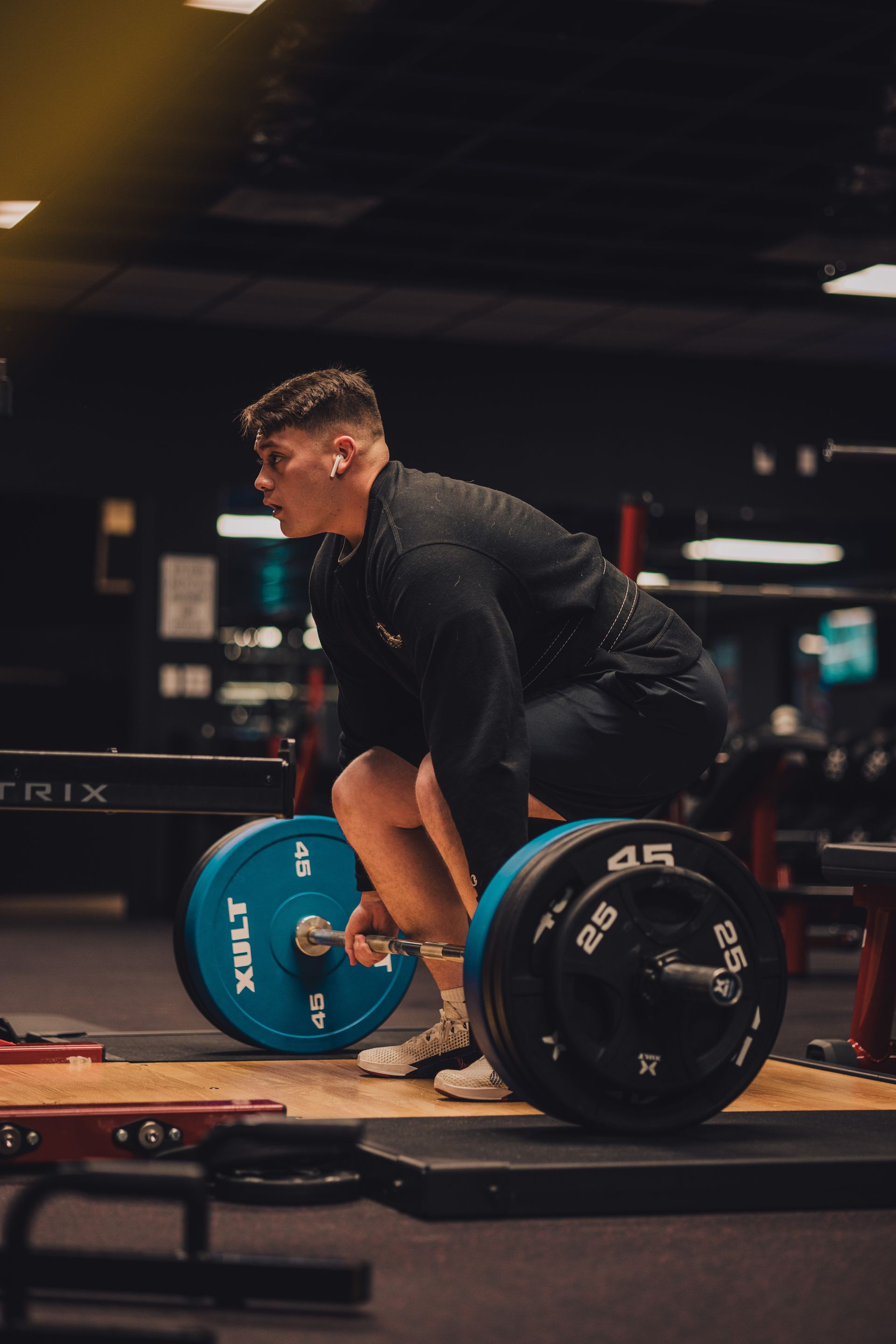 A man is squatting down with a barbell in a gym.