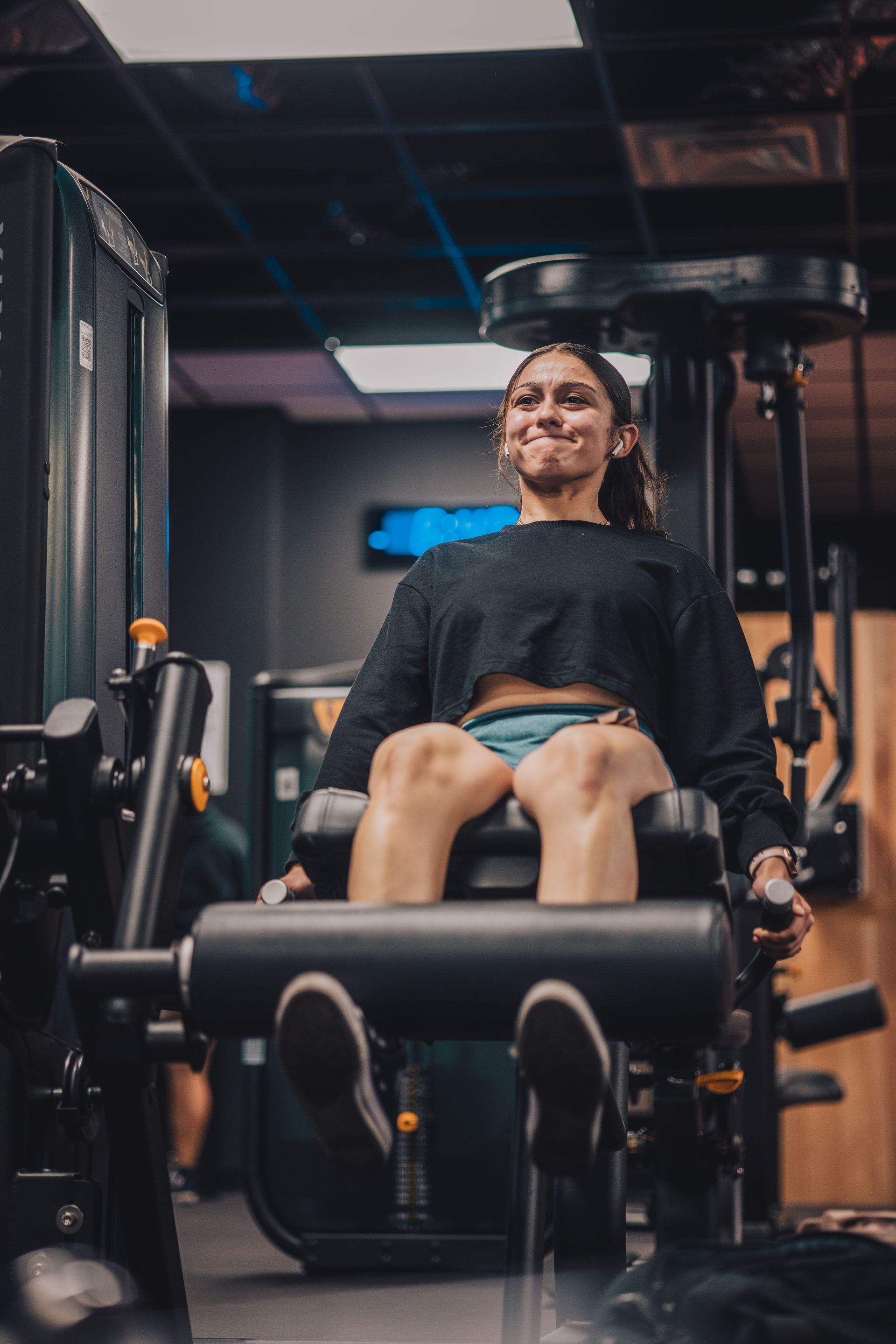 A woman is sitting on a machine in a gym.