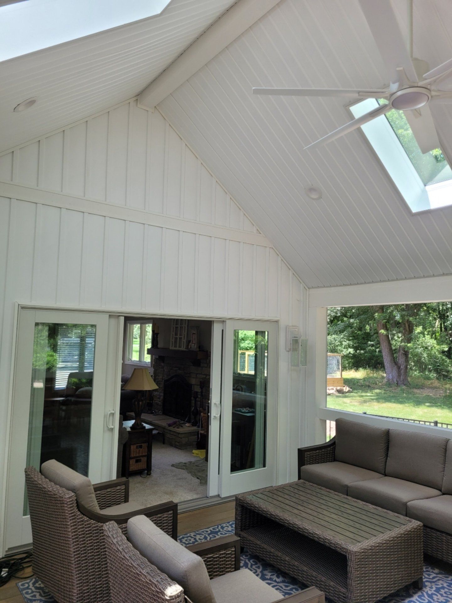 Sunroom interior with white walls, skylight, and outdoor furniture. Doors lead to a living area.