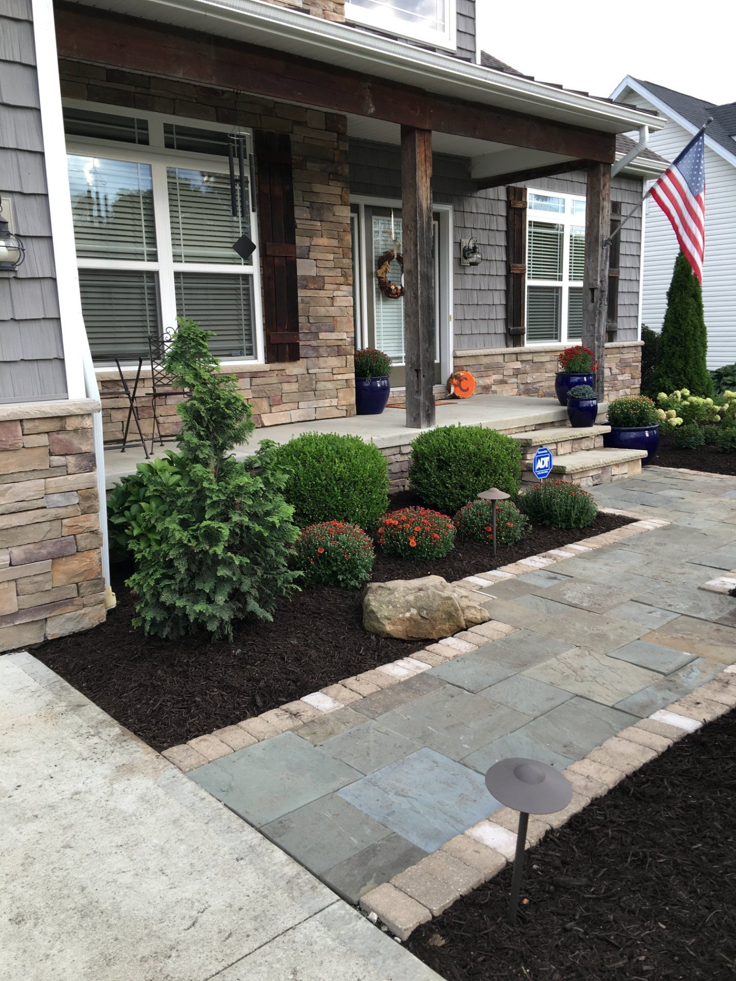 A house exterior with a paved walkway, landscaping, and a porch adorned with an American flag.