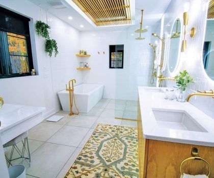Bright, modern bathroom with gold fixtures, white walls, soaking tub, and decorative rug.
