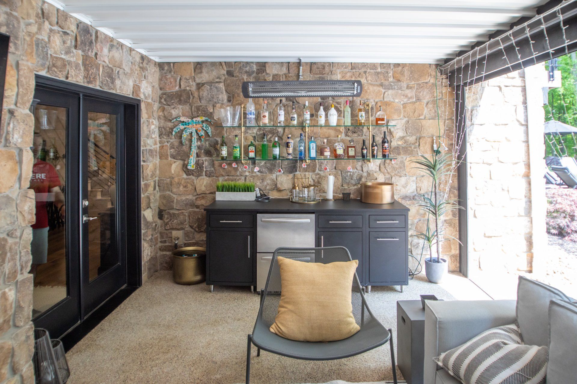 Outdoor bar with stone wall, stocked with liquor, and seating area.