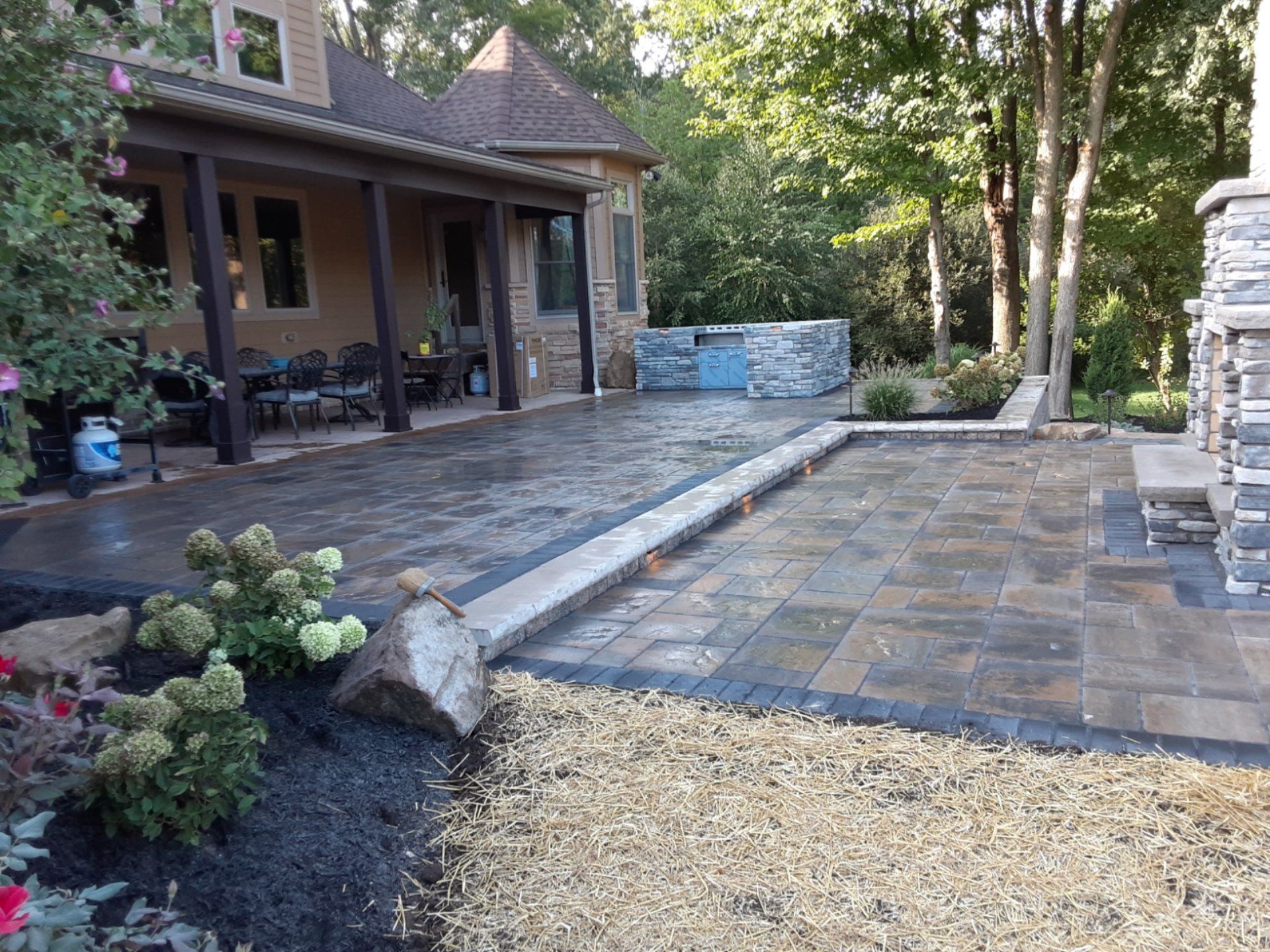Patio with pavers, landscaping, and a house. Blue and brown tones.