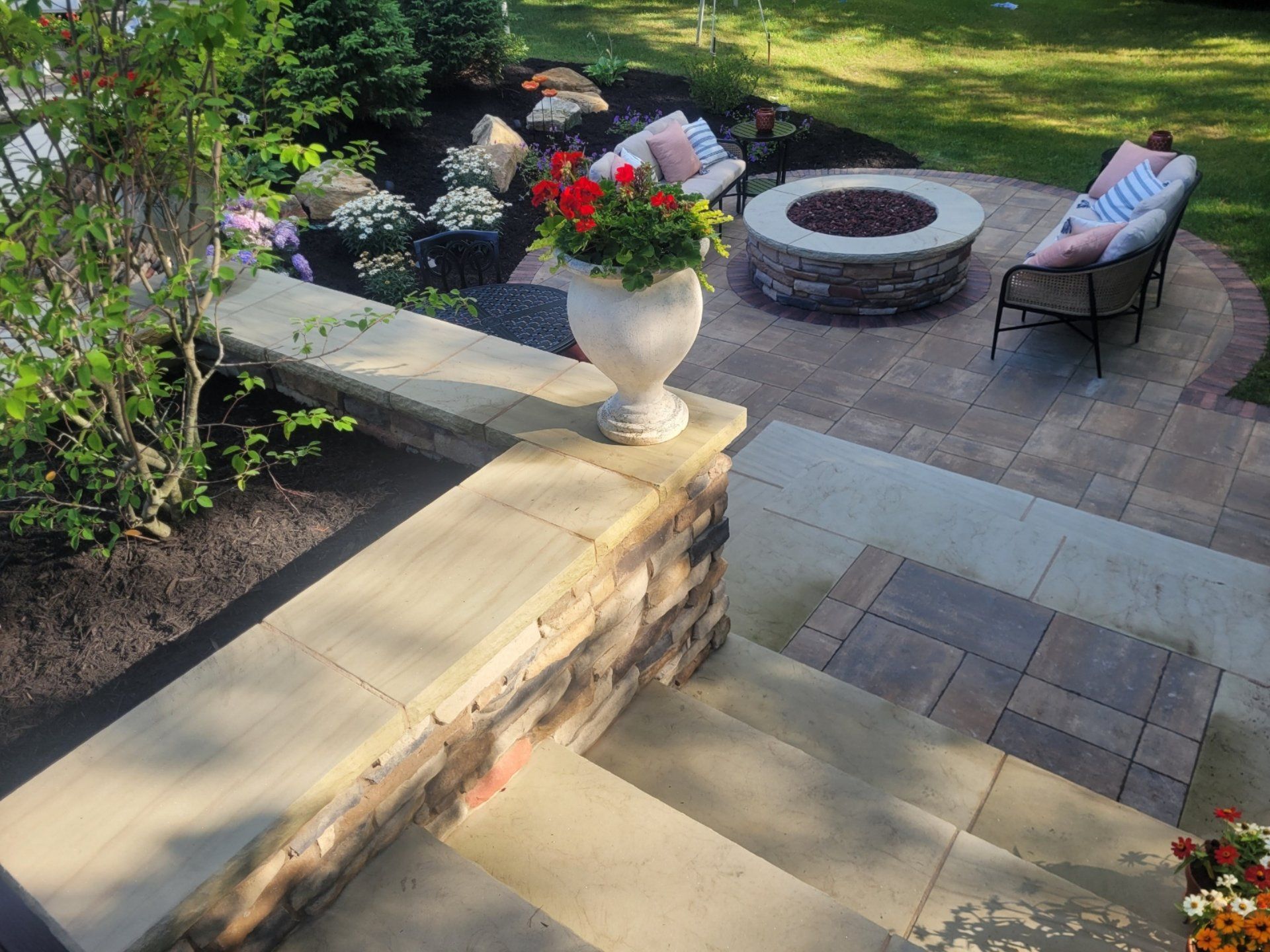 Stone patio with fire pit, seating, and a flower pot.