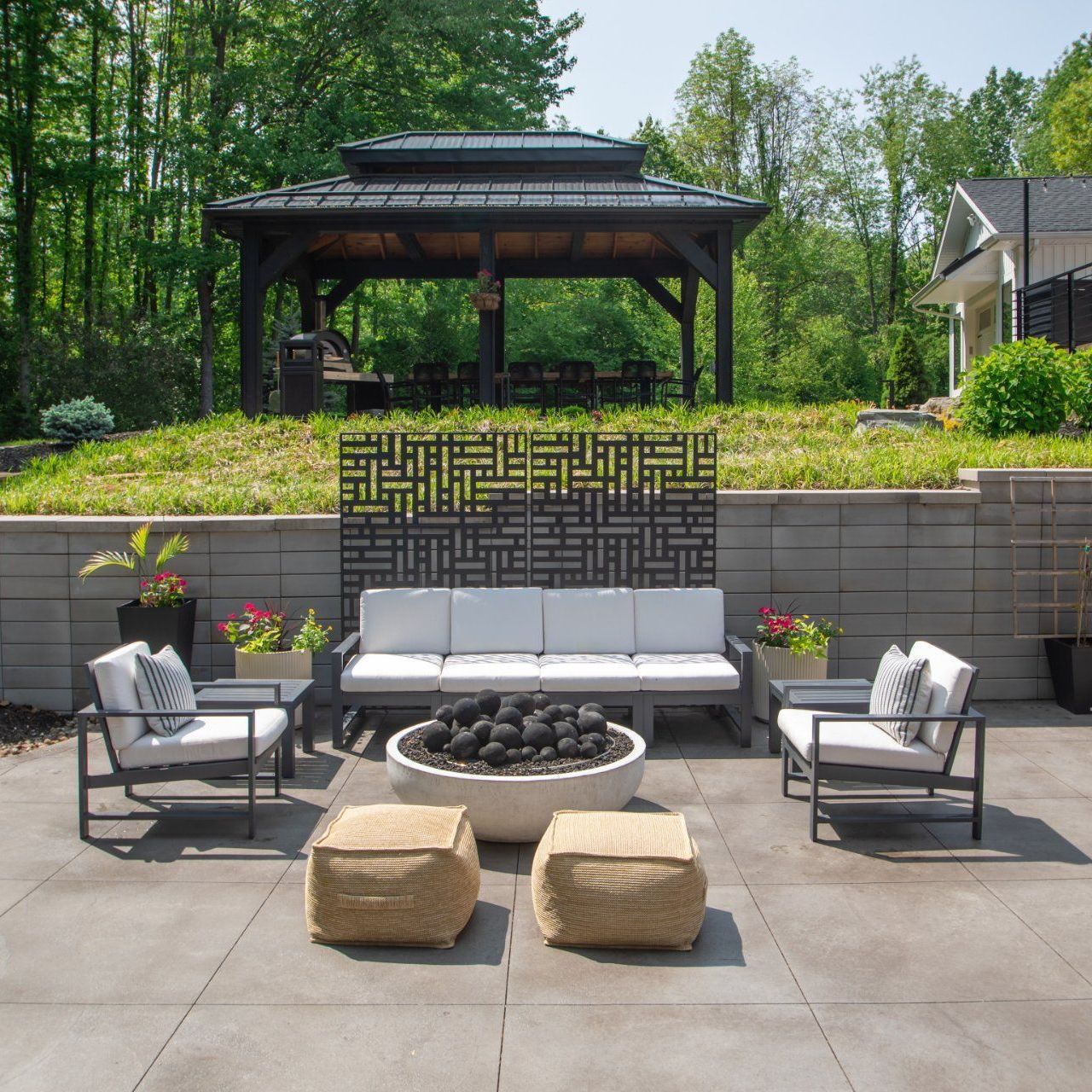 Outdoor patio with seating, fire pit, and gazebo in a backyard setting.