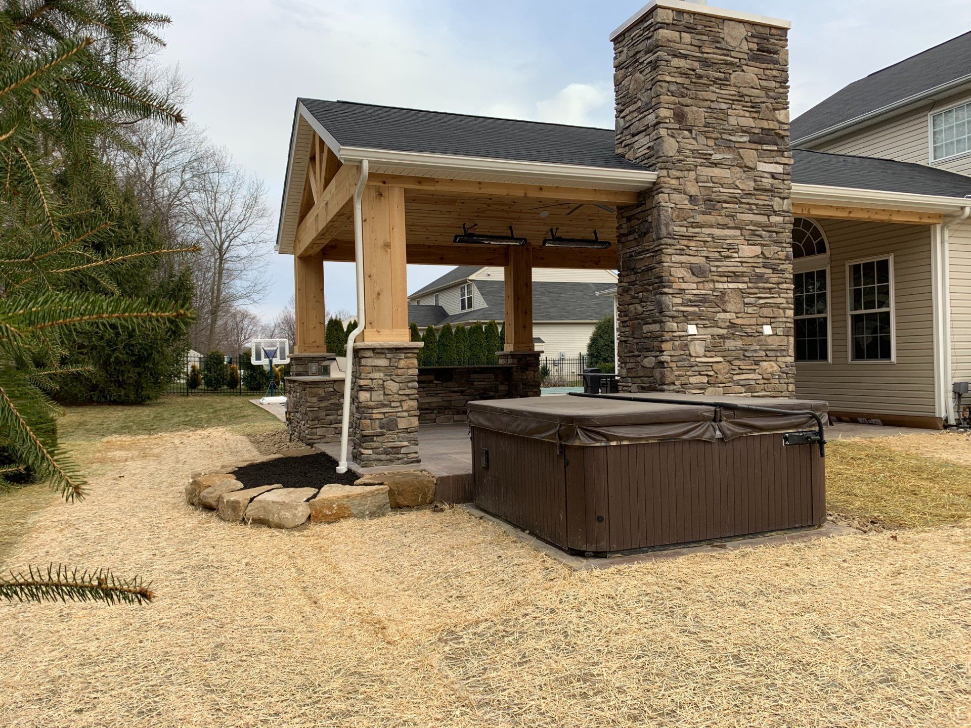Outdoor patio with a hot tub under a wooden pergola and stone chimney.