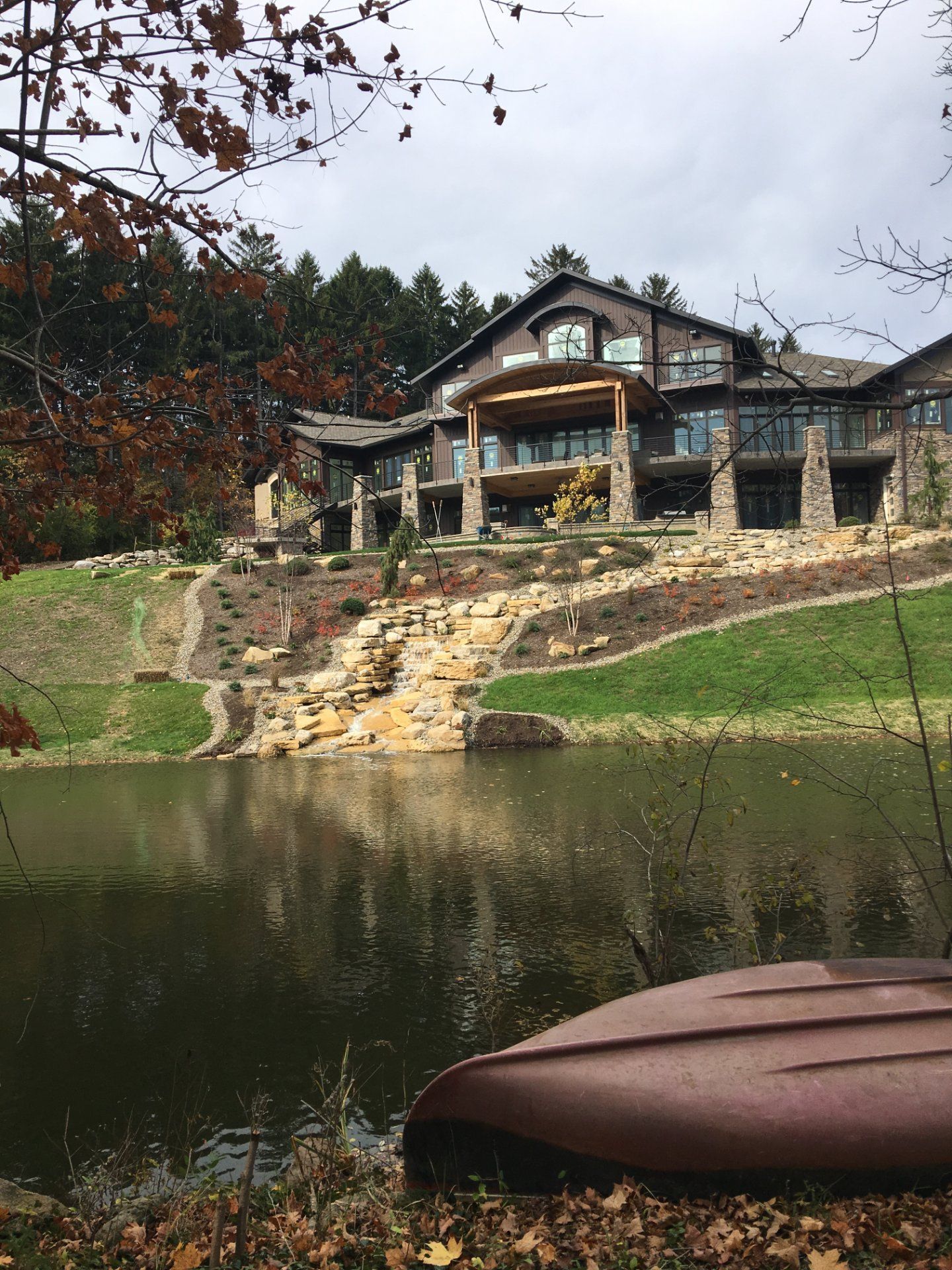 Large house on a hill overlooking a lake; stone and wood construction. A canoe rests in the foreground.