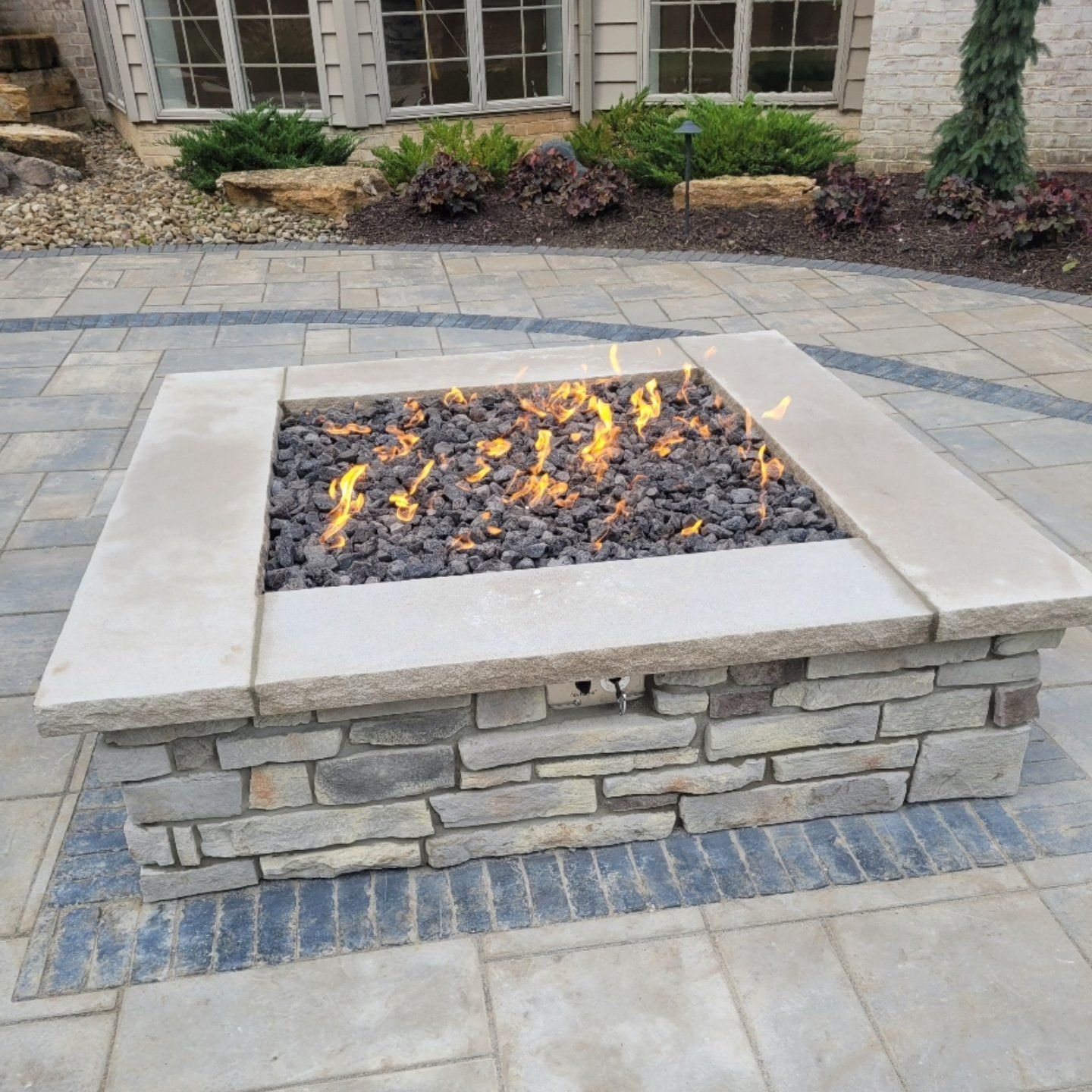 Stone fire pit with flames, in a patio setting.