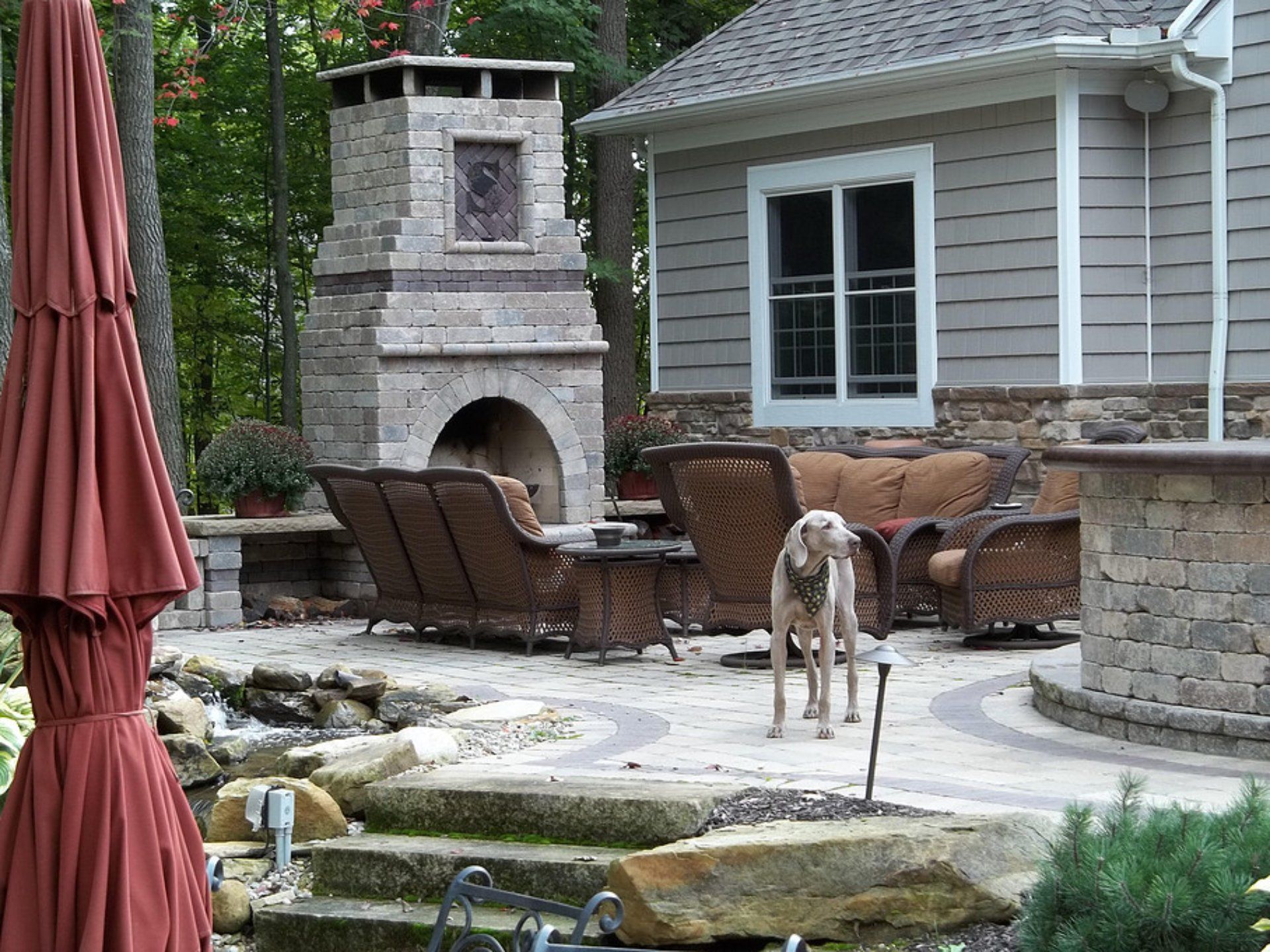 Outdoor patio with a stone fireplace, wicker furniture, and a dog.